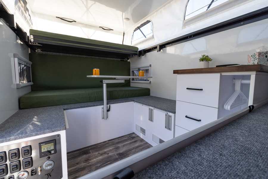 Cozy RV rental interior showcasing a pop-top design with adaptable seating, dining table, and smart storage units.. Teton X Hybrid Comp 2023