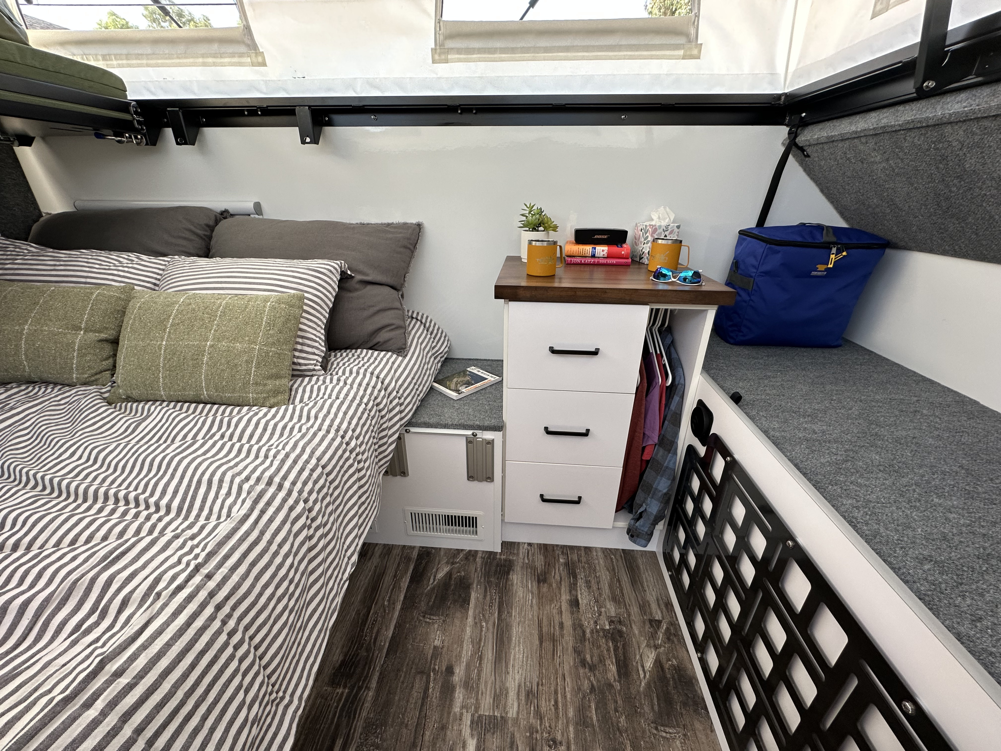Cozy RV rental bedroom with striped bed, practical nightstand, and smart storage bench for a comfortable travel experience.. Teton X Hybrid Comp 2023