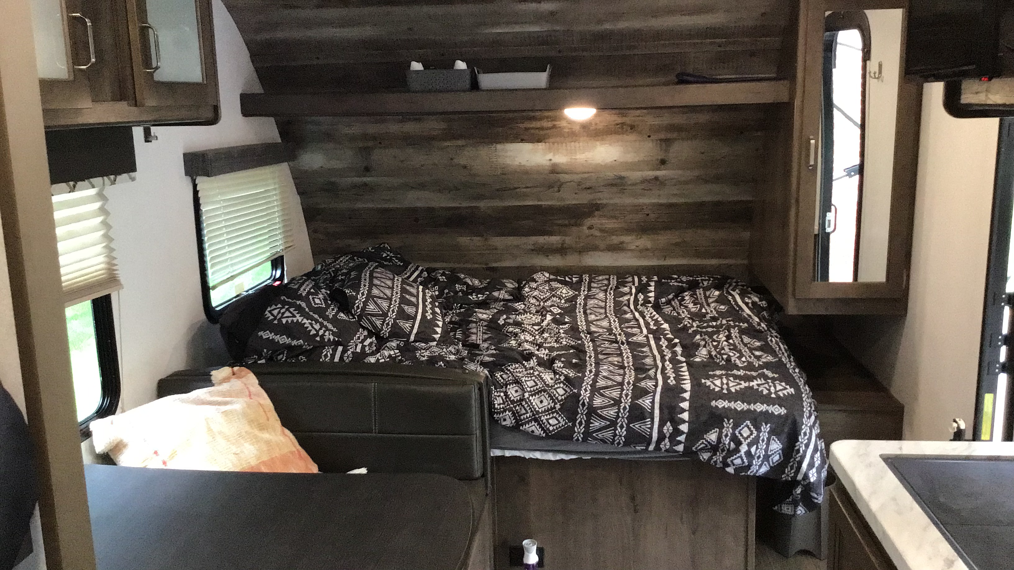Inside a comfy RV rental, featuring a bed with a black & white comforter, windows, and practical storage.. Keystone RV Passport Express 2019