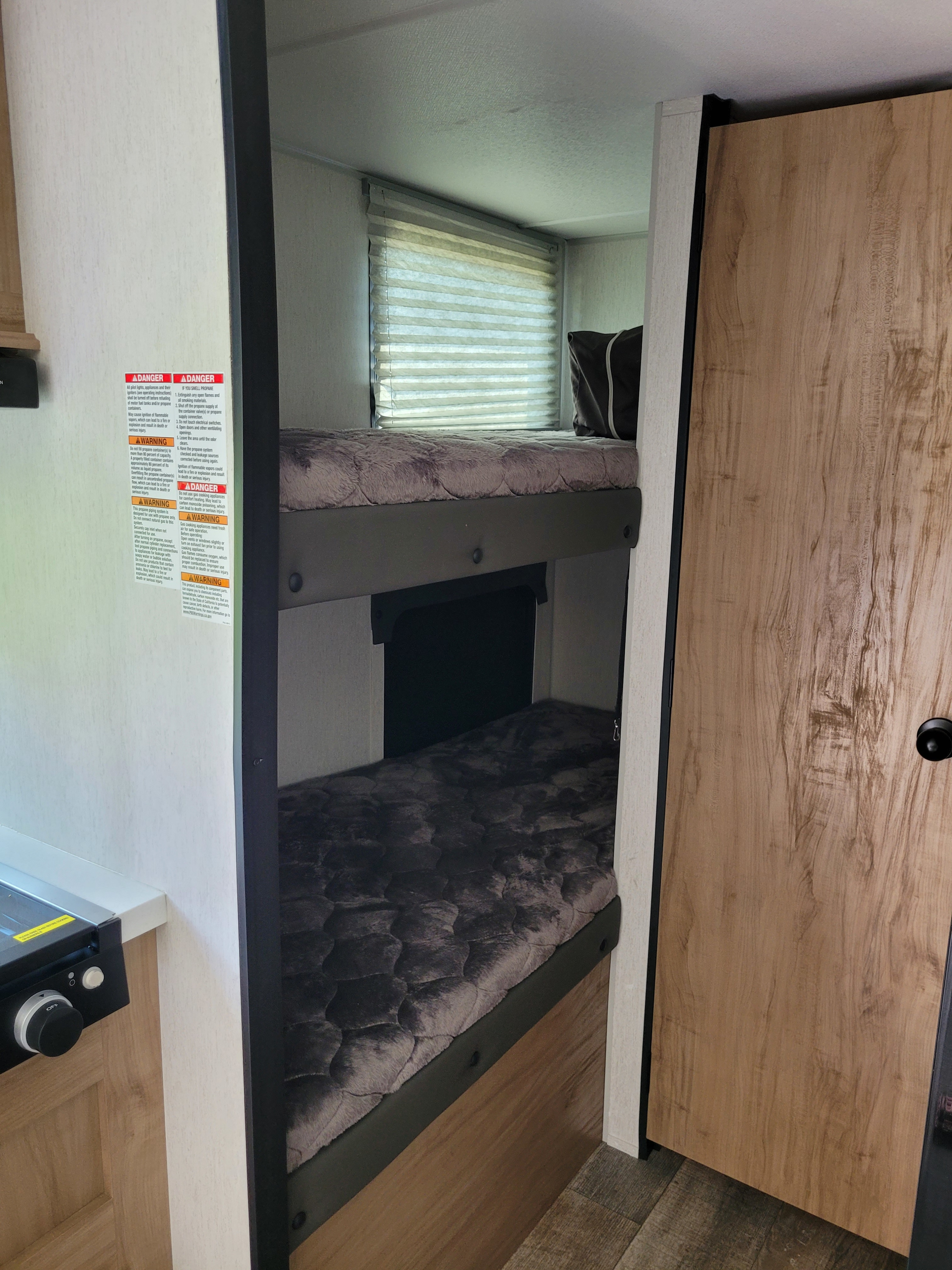 View of bunk beds in an RV rental, showing safety labels and window blinds in the interior.. Forest River 17JG 2023