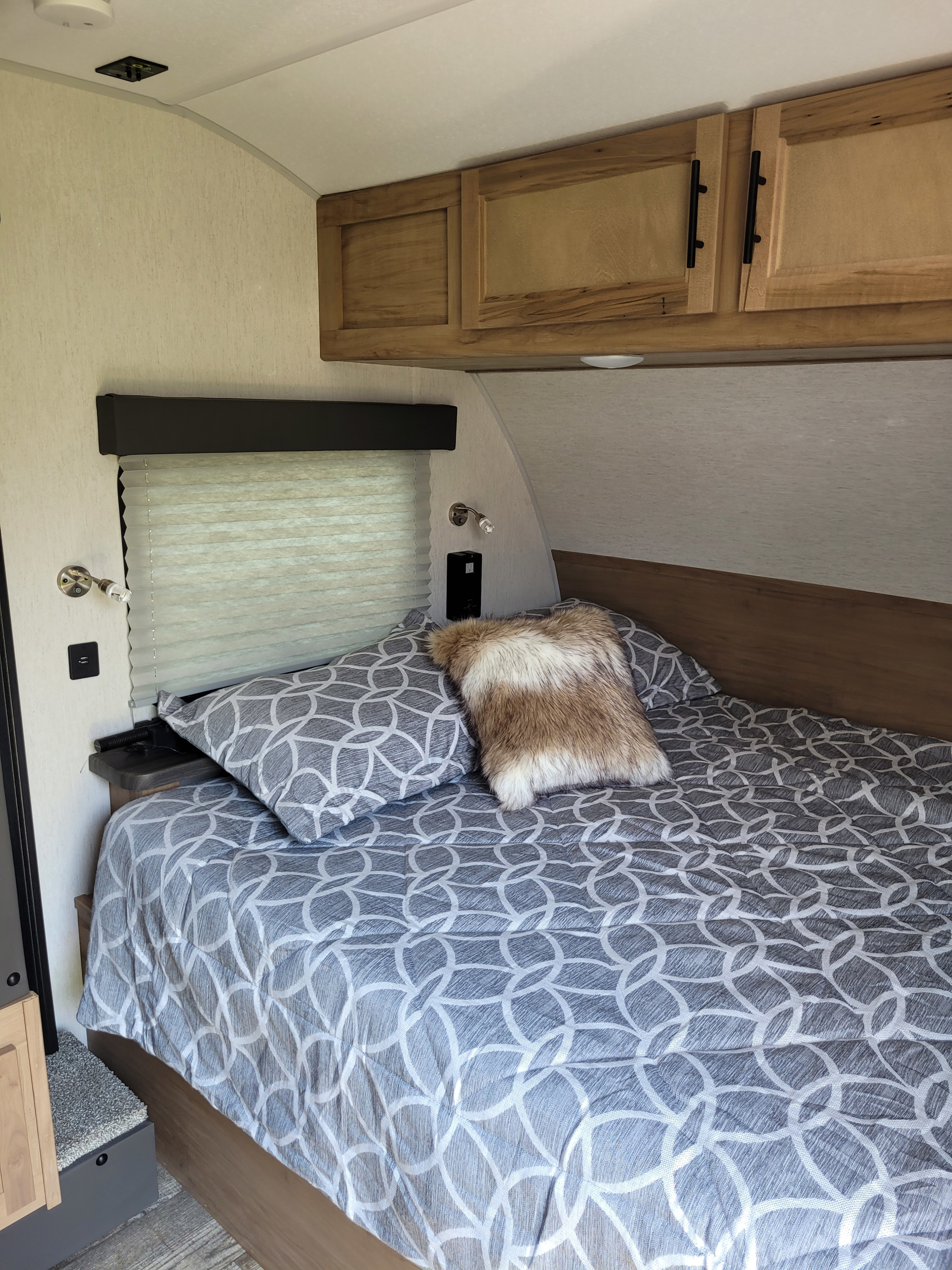 RV rental: A cozy bedroom with patterned bedding, overhead cabinets, and a window with shade, offering comfort for travel.. Forest River 17JG 2023
