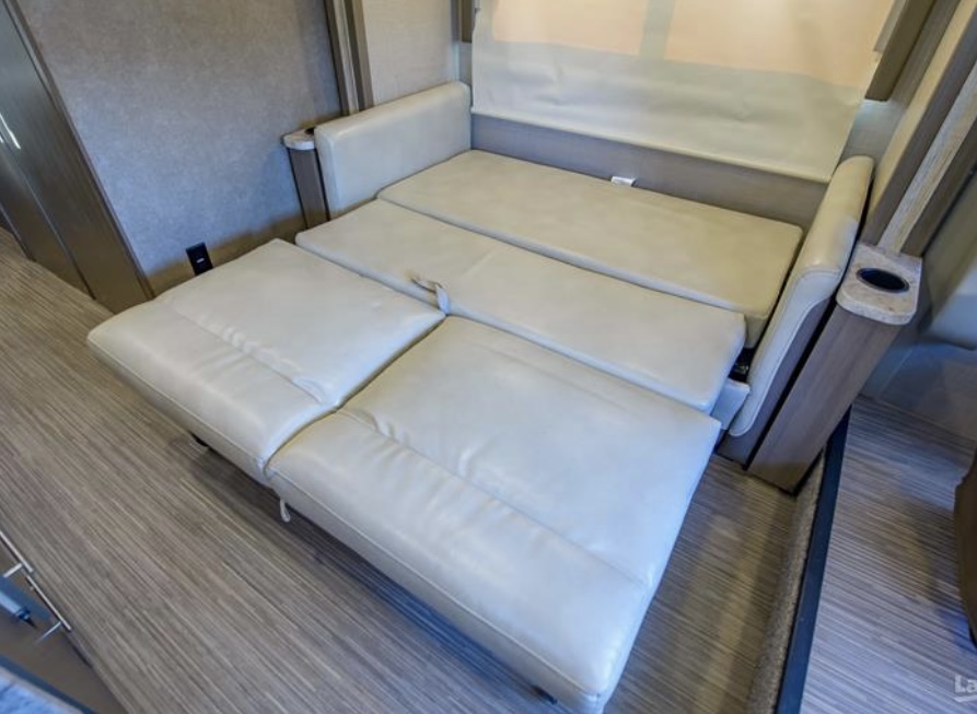 An RV rental's cream sofa sleeper extends, demonstrating versatile seating and sleeping in a compact space.. Thor Vegas 2018