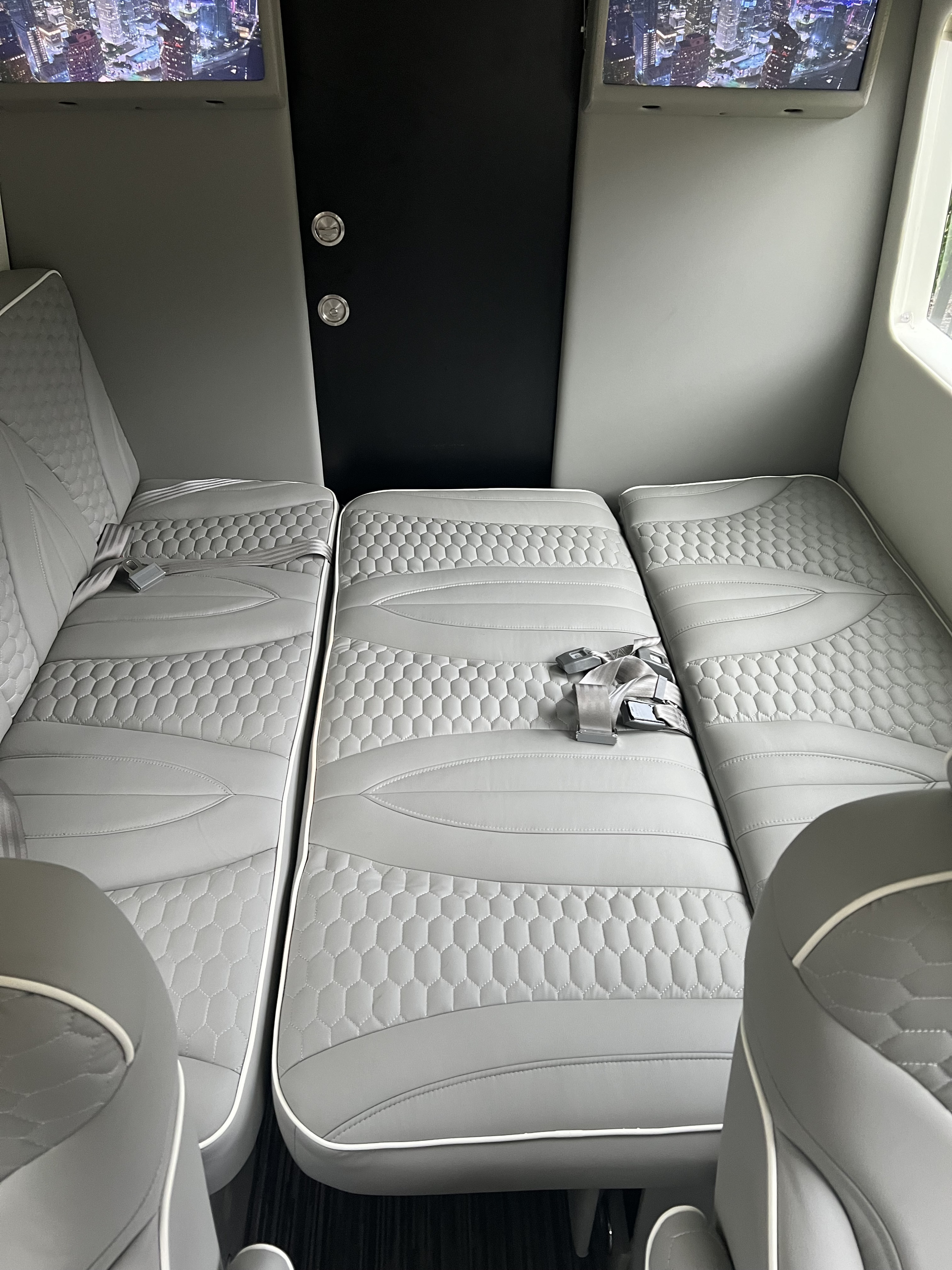 Spacious RV rental interior with three plush, grey seats convertible to beds, overhead screens & stylish quilted design.. Other Sprinter 2022