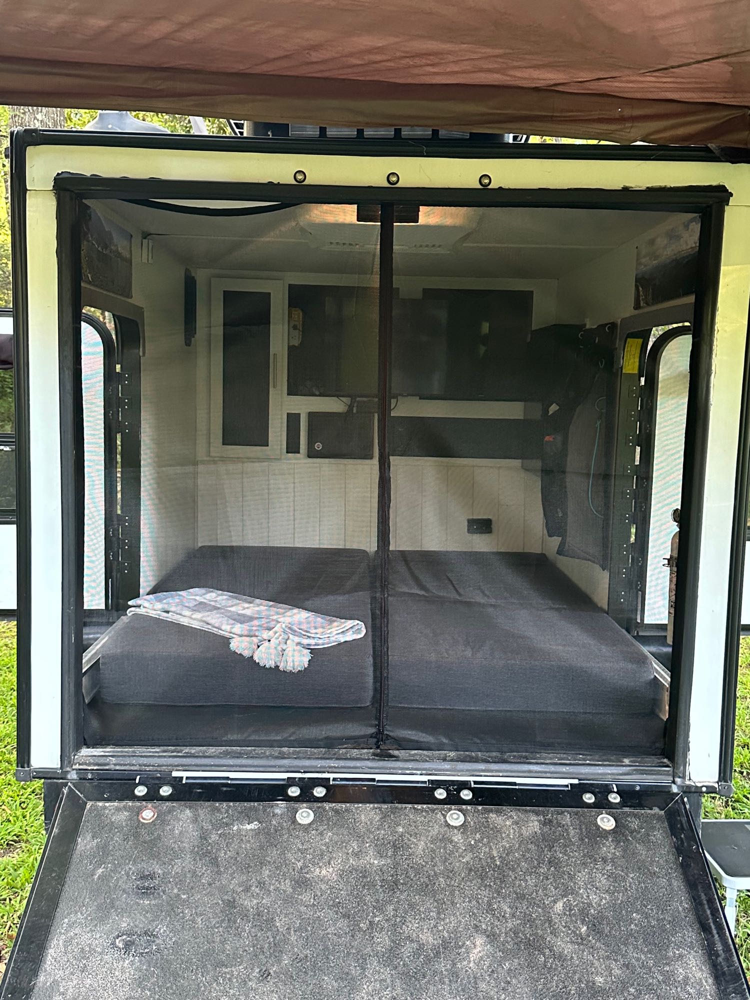 Rear view inside an RV rental shows a comfy bed, mesh screen door, and built-in storage for travel & camping.. Forest River No Boundaries 10.6 2017