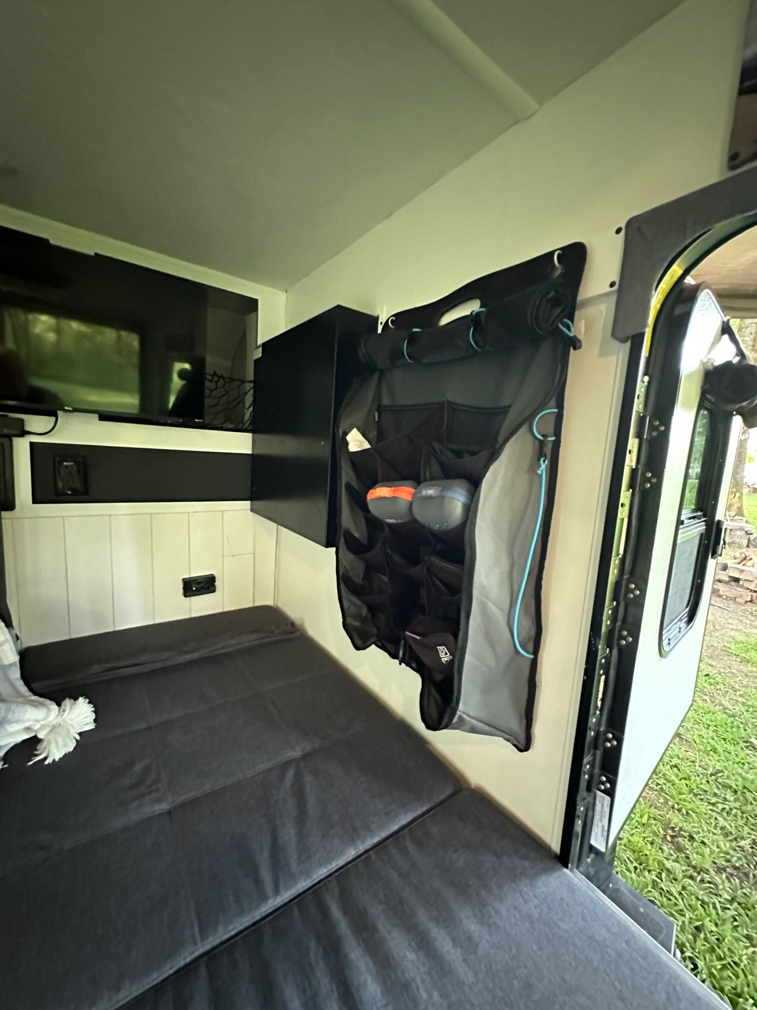 RV rental interior features a compact bed, wall-mounted TV, and a convenient hanging storage organizer near the open door.. Forest River No Boundaries 10.6 2017