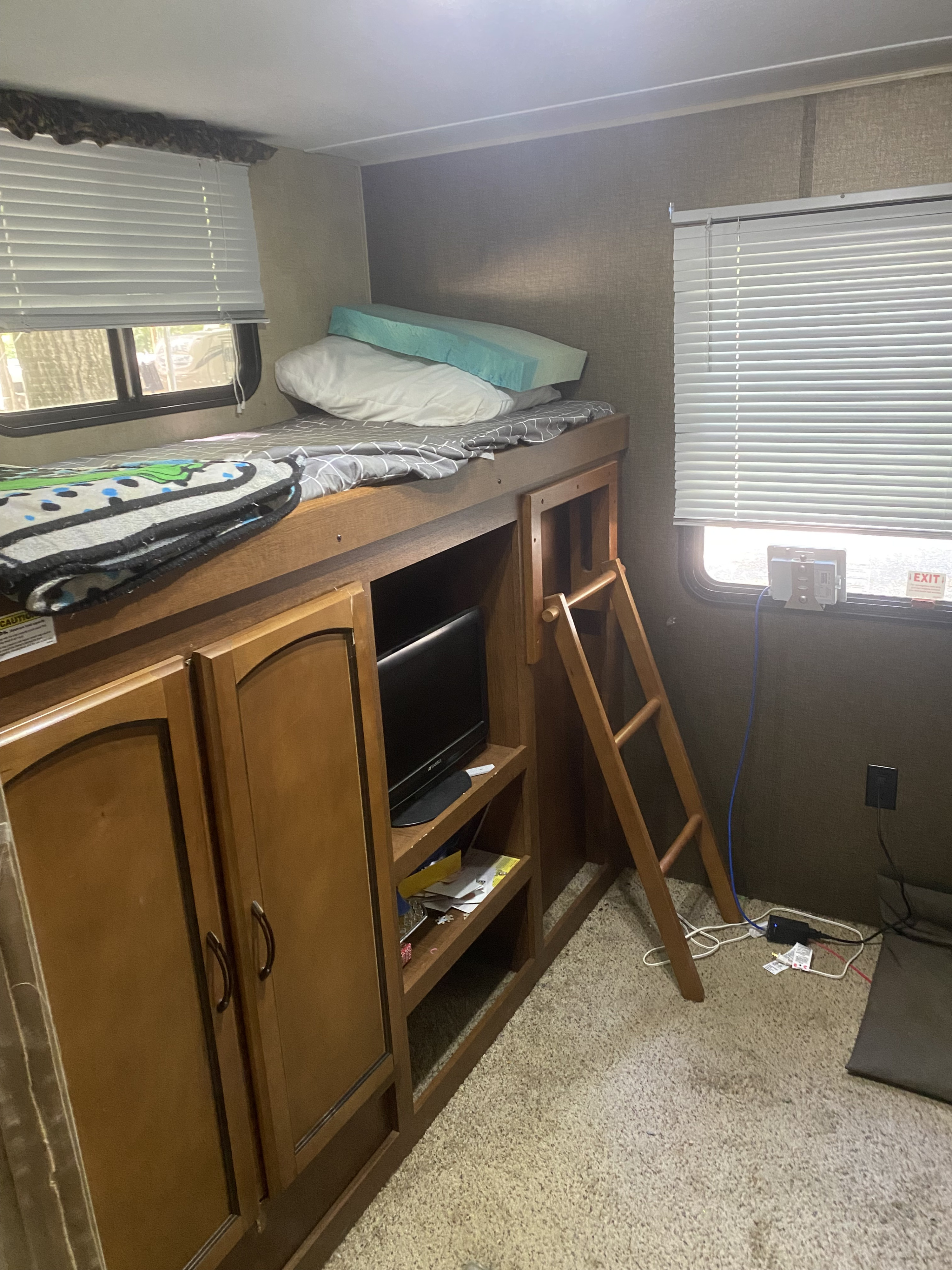 Cozy RV rental bunk bed setup with integrated storage, TV, and ladder. Ideal sleeping area for campers.. Keystone RV Summerland 2015