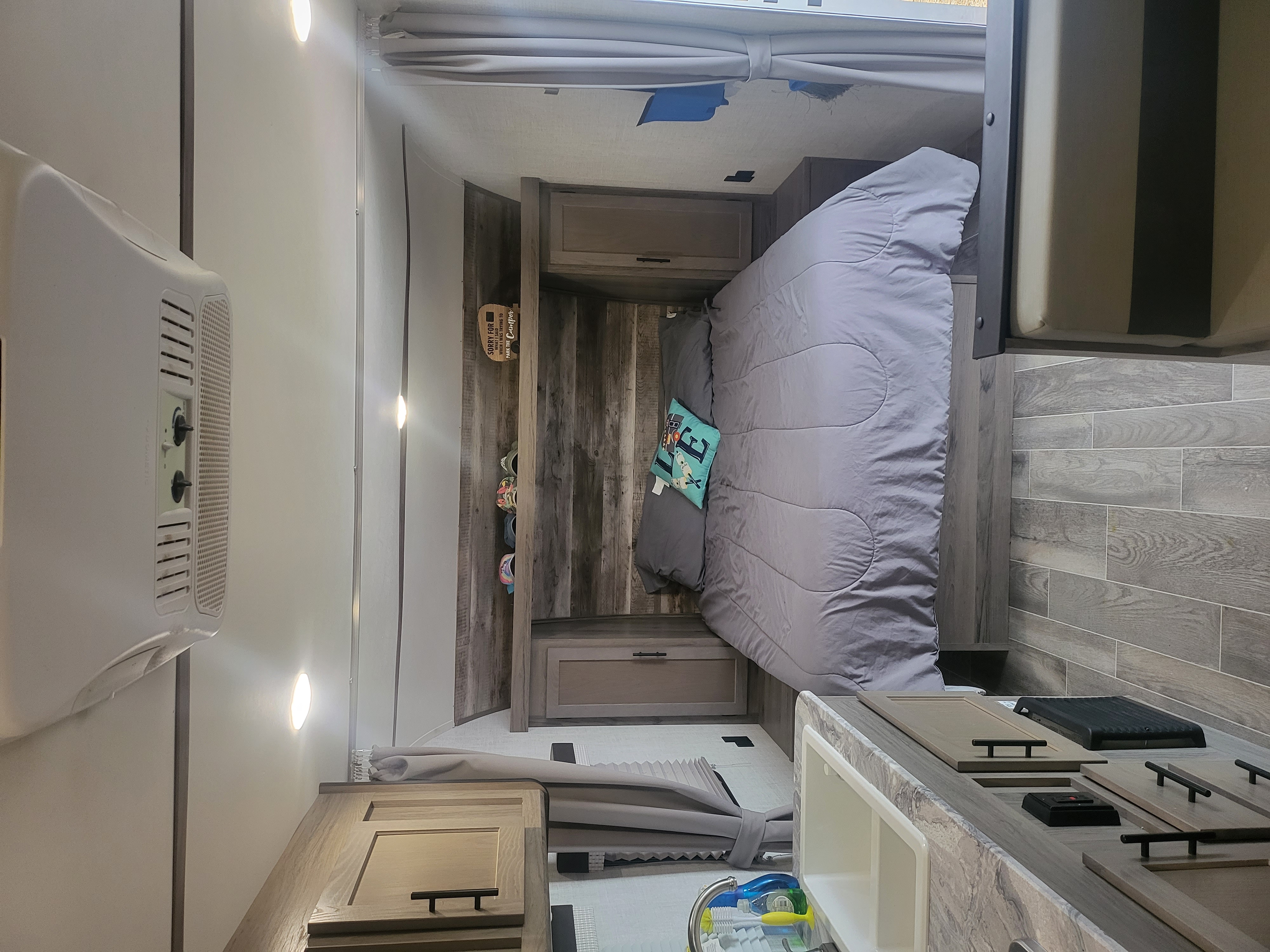 Inside a comfy RV rental: a modern bedroom with a bed, cabinets, and a humorous camper parking sign.. Gulf Stream Enlighten 2021