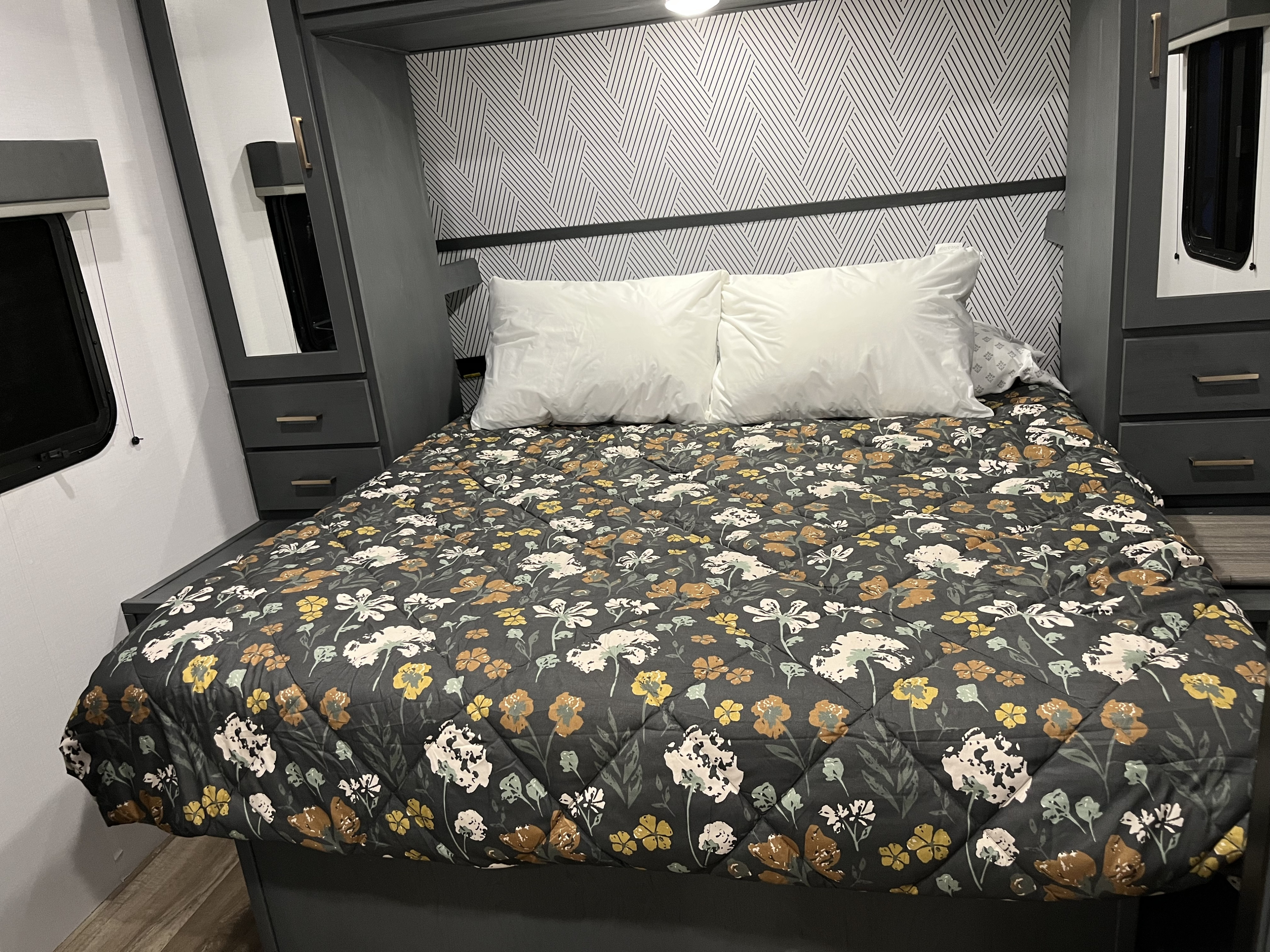 Cozy RV rental bedroom features a floral comforter, white pillows, and built-in storage for a comfortable stay.. Keystone RV Bullet Ultra Lite 2022