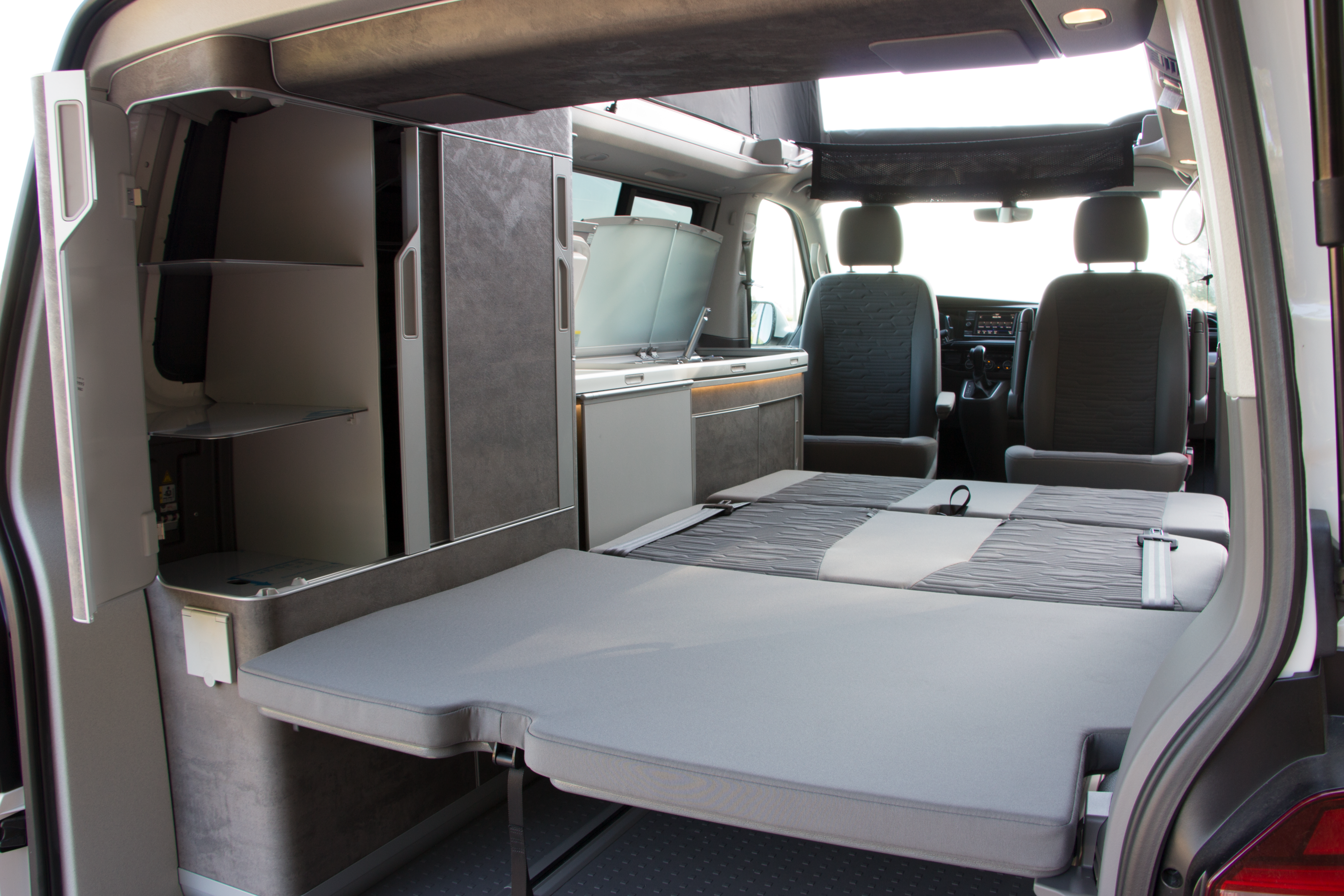 Explore this RV rental camper van interior: convertible bed/seating, compact kitchen, and built-in storage solutions.. Volkswagen CALIFORNIA 2023