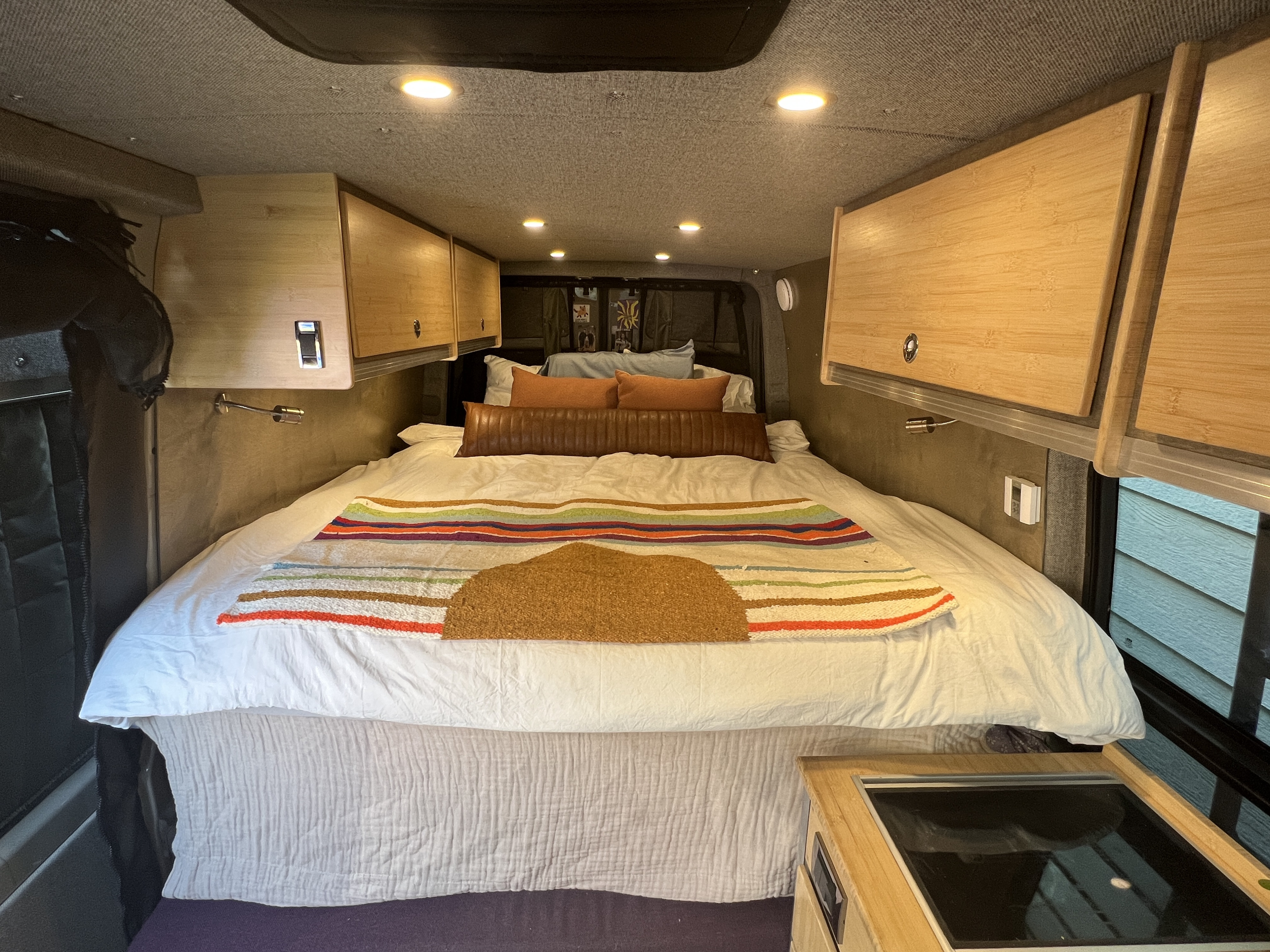 A bright, organized RV rental interior features a comfortable bed, wooden overhead cabinets, and integrated cooktop.. Mercedes Benz Sprinter Van 2017