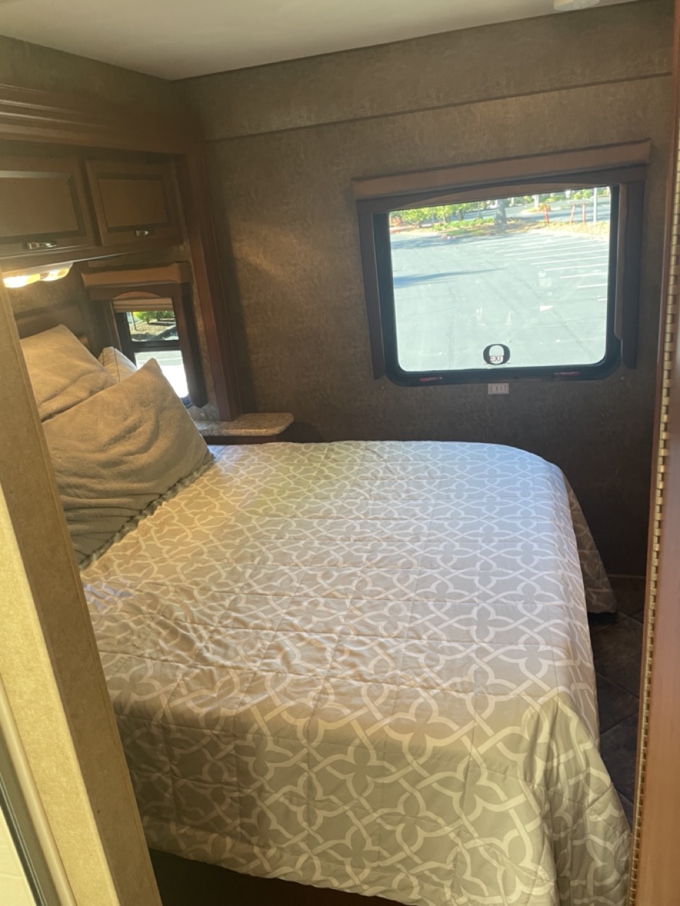 Cozy RV rental bedroom featuring a patterned bedspread, storage cabinets, and a window with a view. Ideal for comfortable travel.. Thor A.C.E. 30.1 EVO 2014