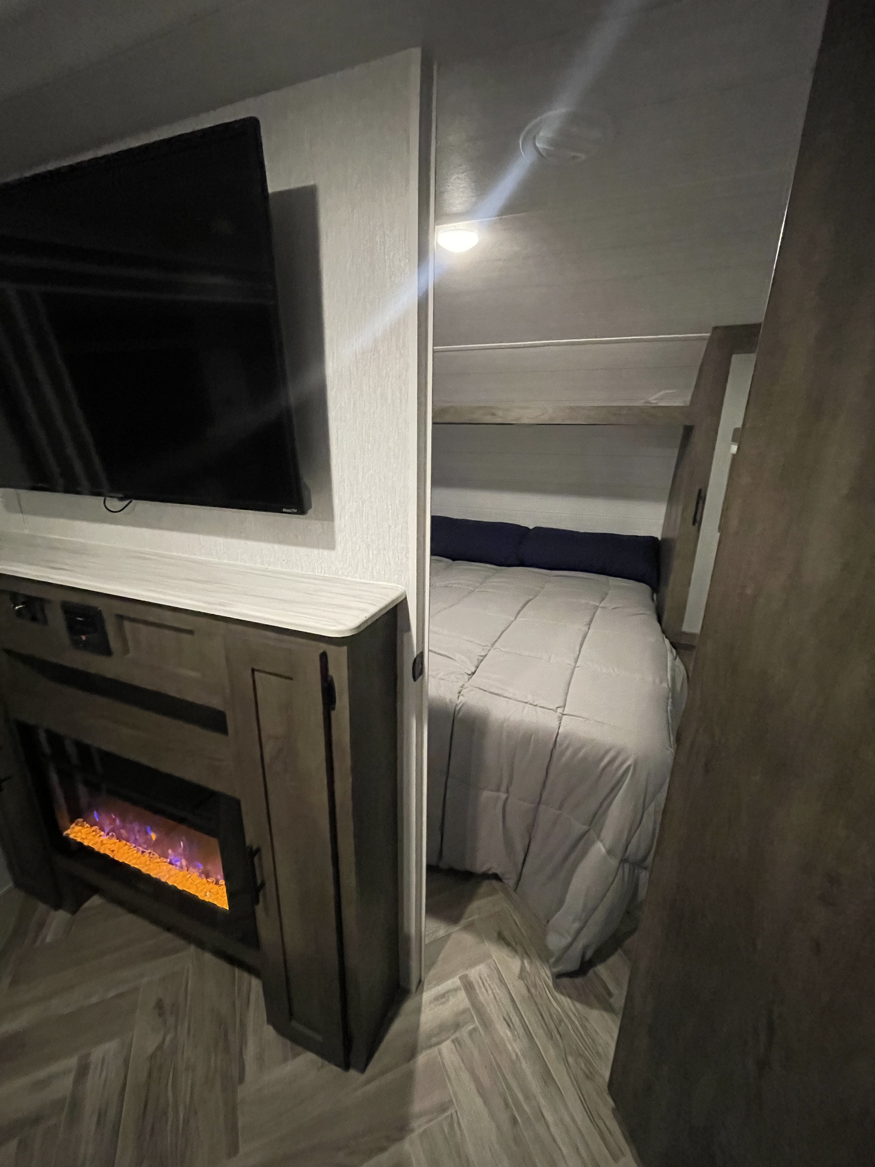 Cozy RV rental interior showing a TV, electric fireplace, and a sleeping alcove with a bed and top bunk. Compact setup.. Forest River Salem Cruise Lite 2022