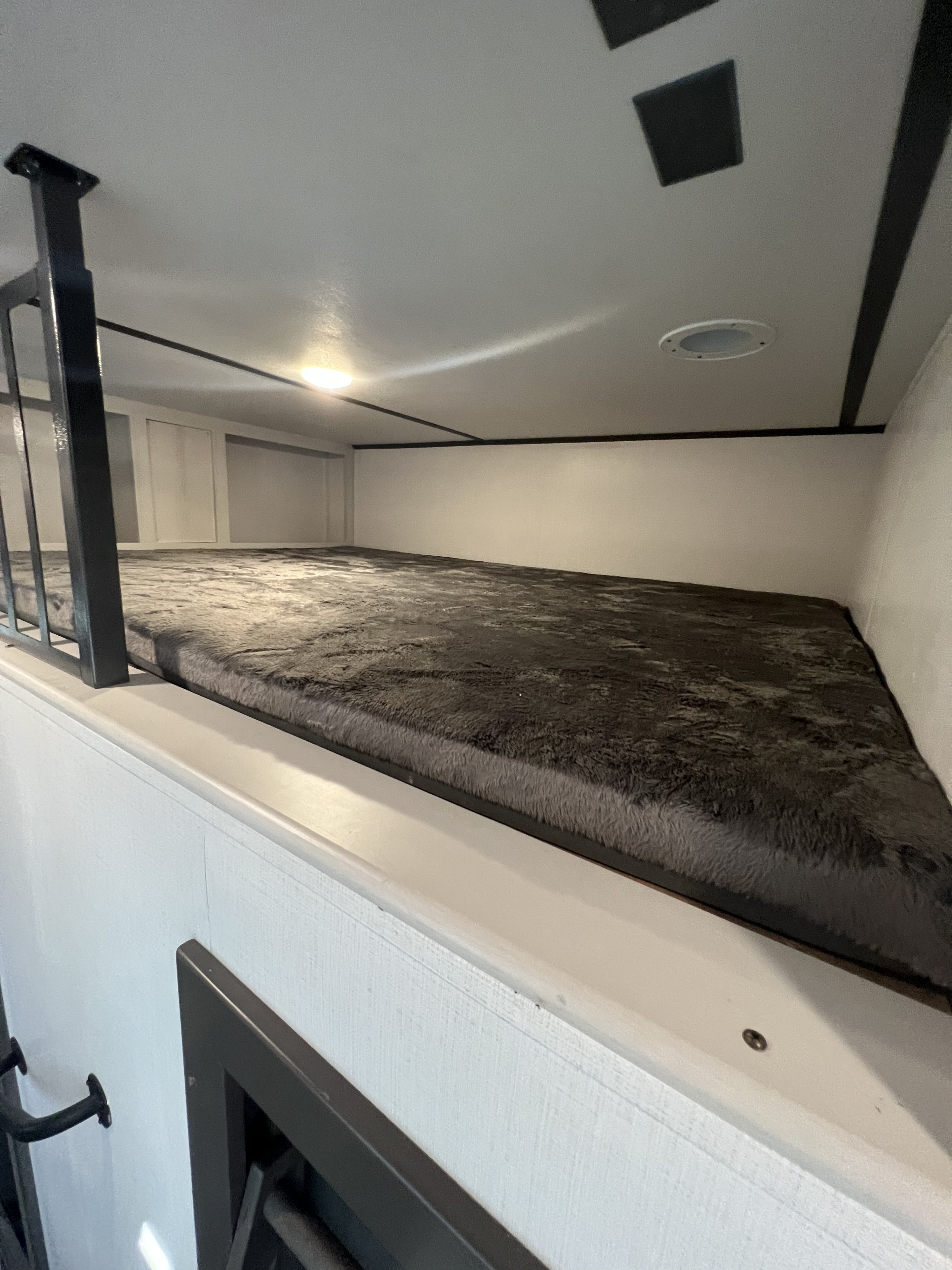 Cozy RV rental bunk bed area featuring a large grey fuzzy mattress, metal safety railing, and ample wall storage. Ideal for travelers.. Keystone Sprinter 2023