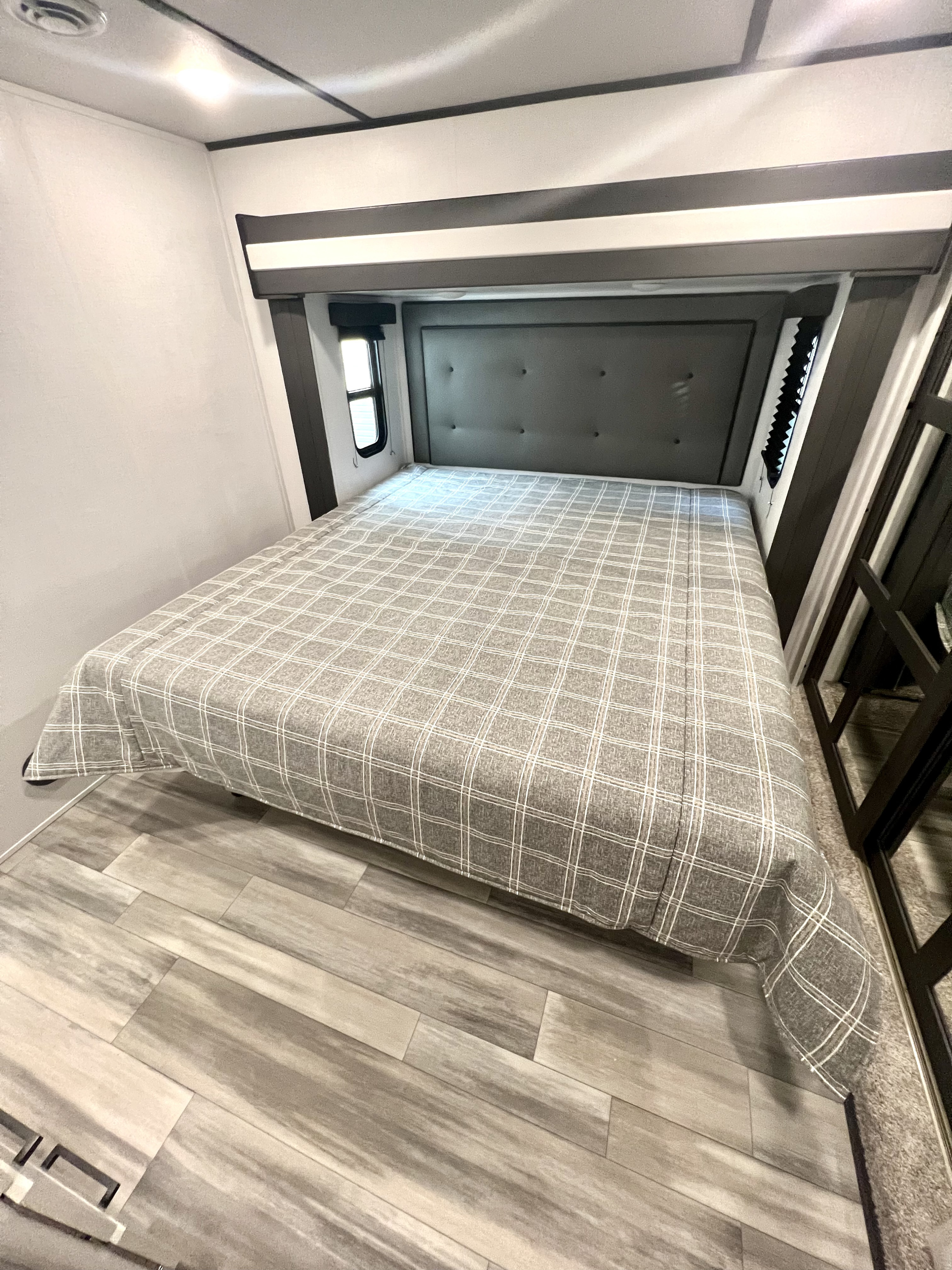 This RV rental offers a compact, modern bedroom with a queen-sized bed, padded headboard, windows, and wood-look flooring.. Keystone Sprinter 2023