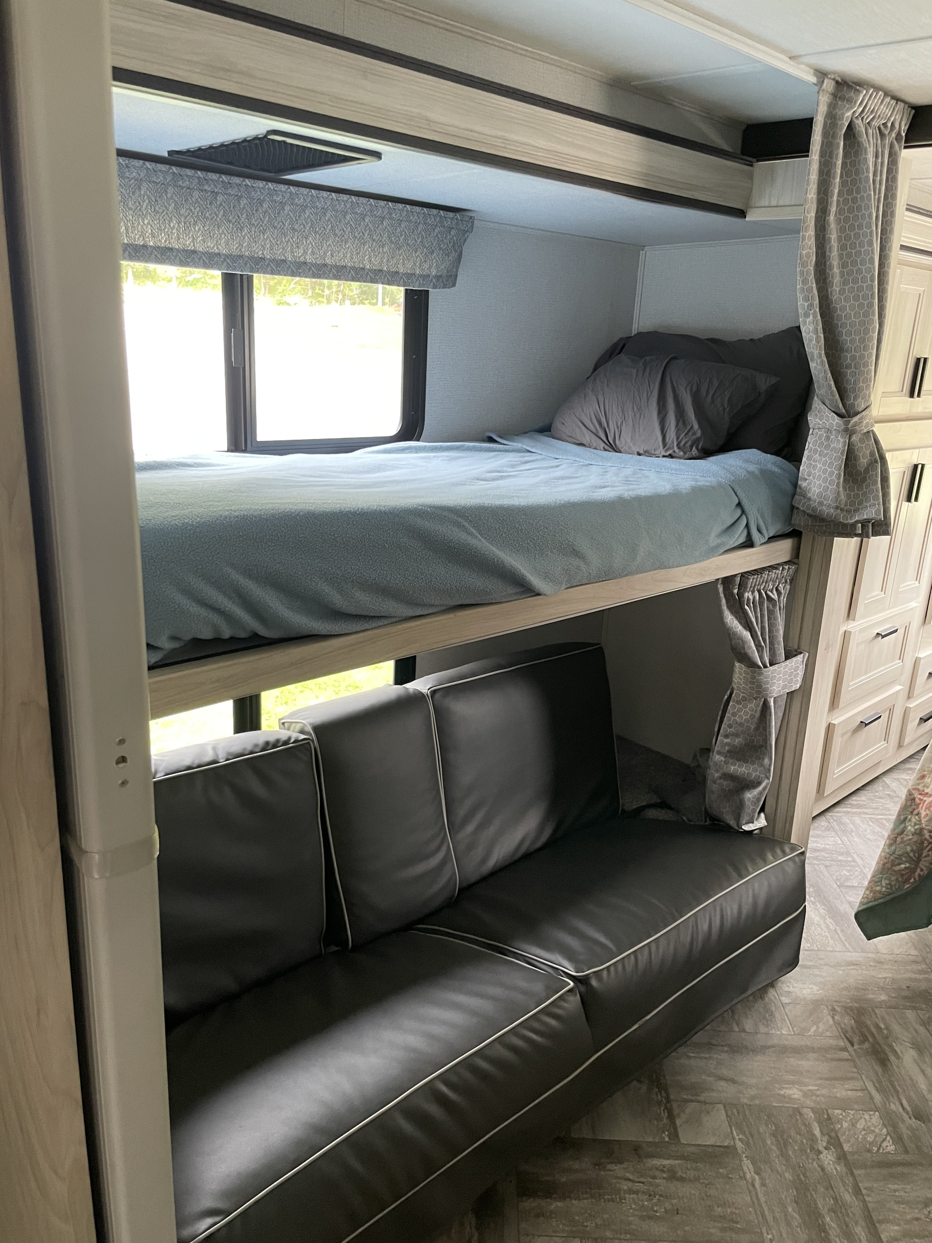 RV rental interior featuring a cozy bunk bed over a sleek black sofa, with a bright window and built-in storage.. Forester LE 2022