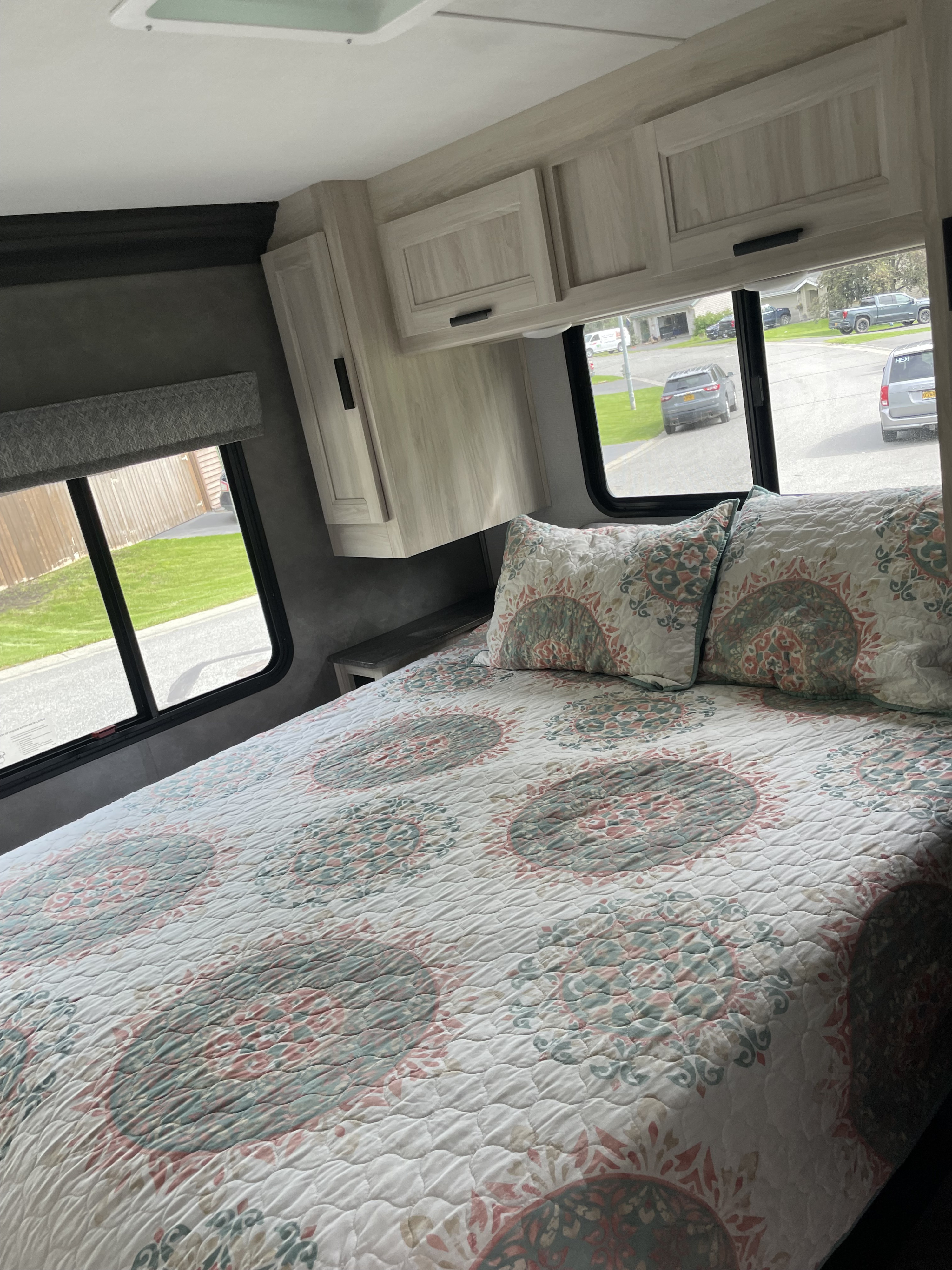 Cozy RV rental bedroom with patterned quilt, overhead cabinets, and large windows looking onto a residential street.. Forester LE 2022