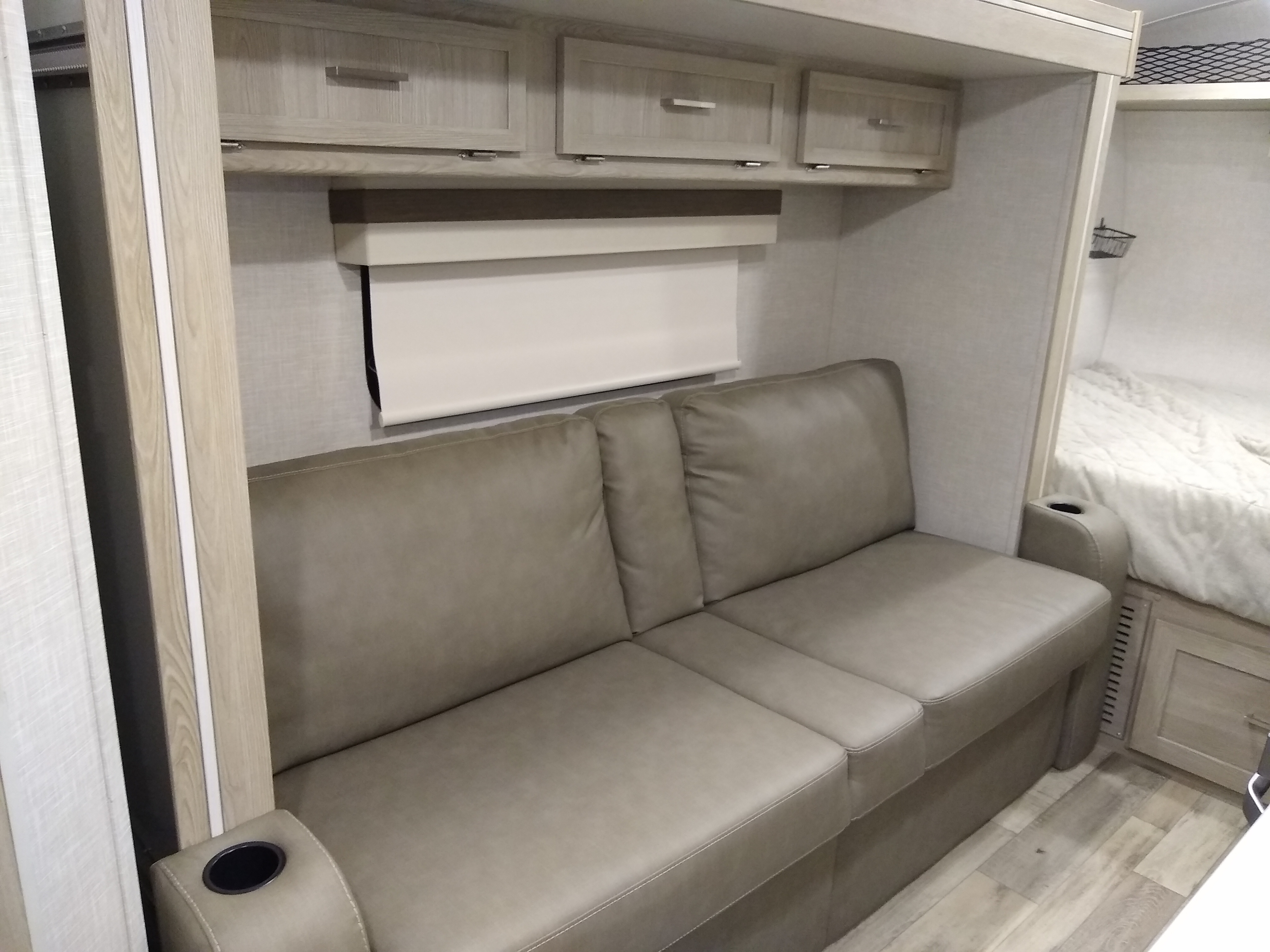Modern RV rental interior with a light-toned sofa and cup holders, storage cabinets, and a bedroom area visible.. Forest River Rockwood Geo Pro 2022
