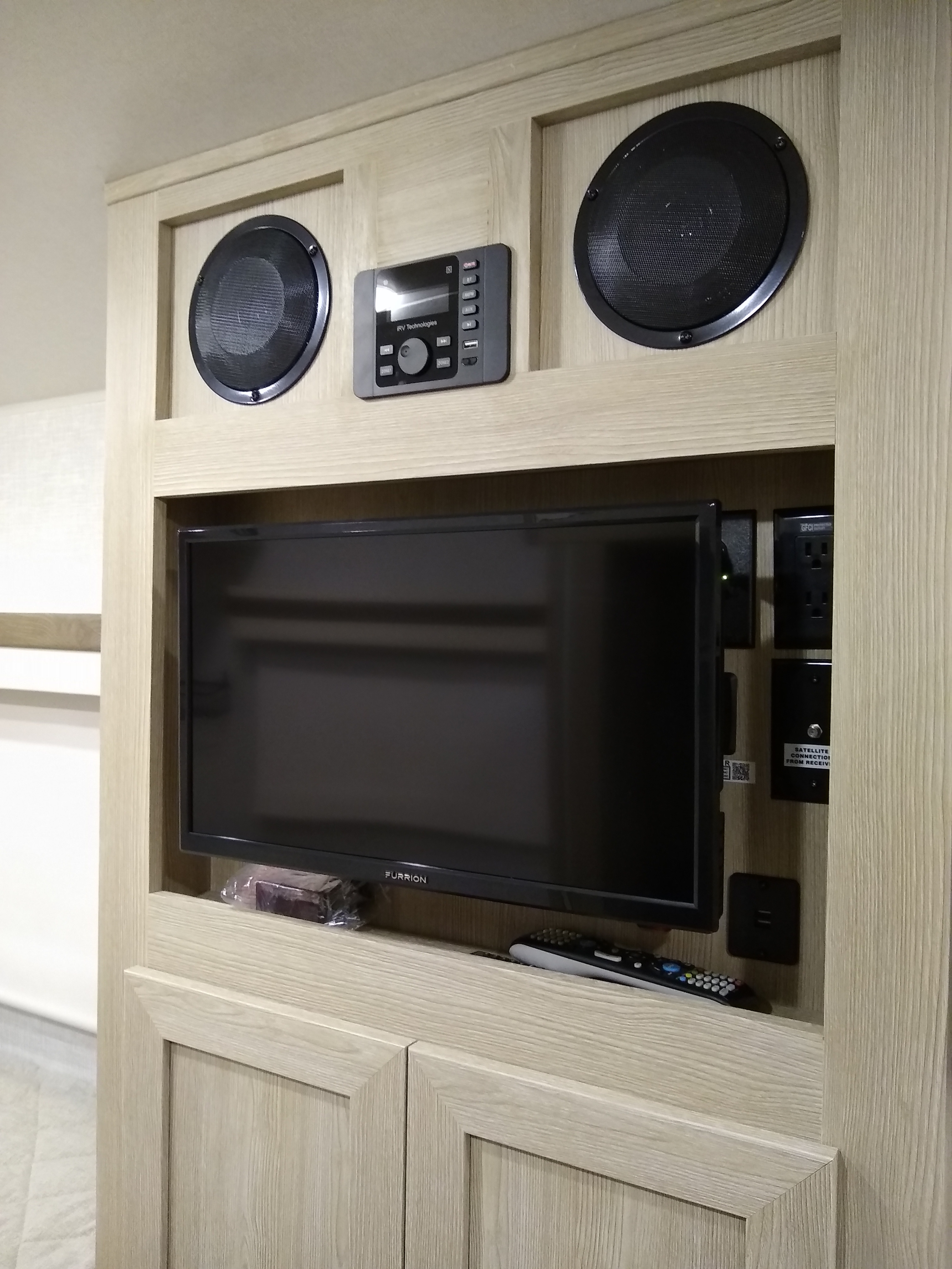 Inside an RV rental: a modern entertainment center with Furrion TV, speakers, and control panel built into wood cabinetry.. Forest River Rockwood Geo Pro 2022