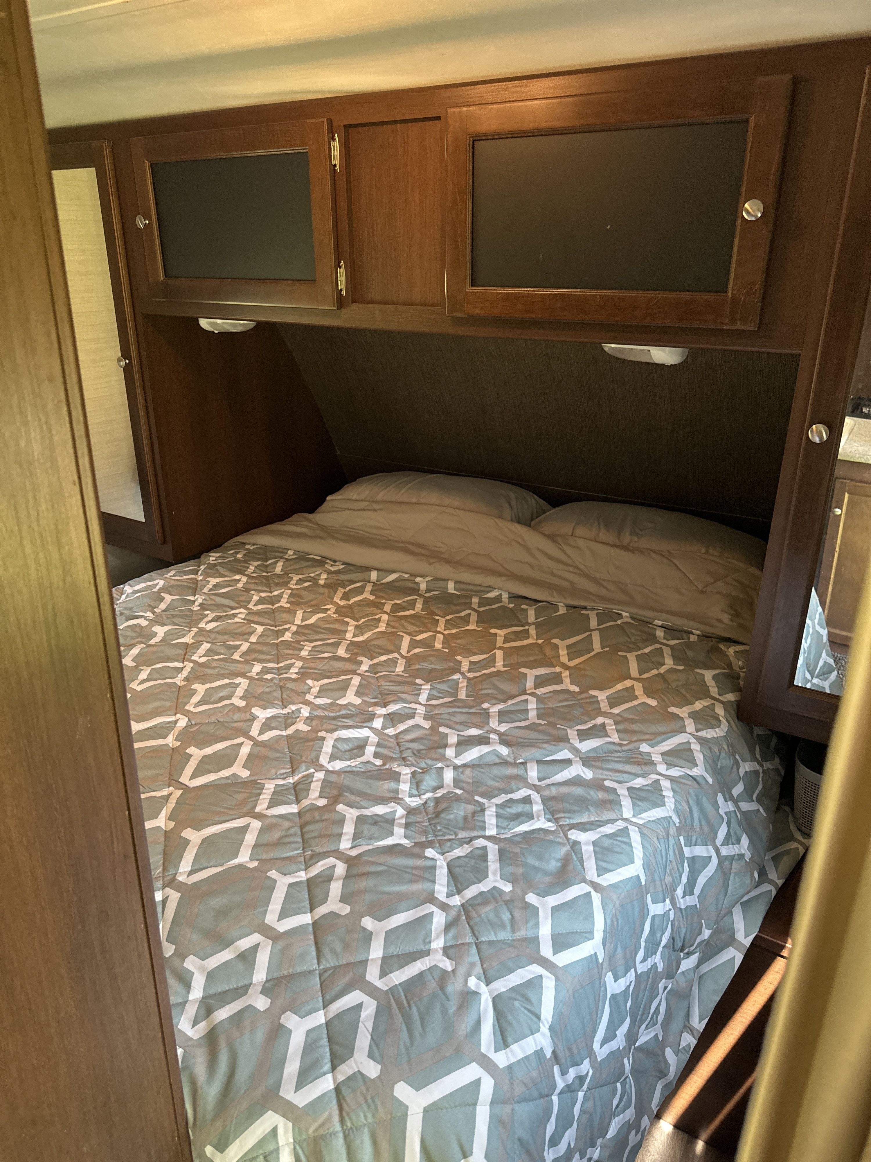 RV rental bedroom with bed, patterned comforter, pillows, and wooden overhead cabinets with built-in lights.. Keystone RV Bullet Ultra Lite 2015
