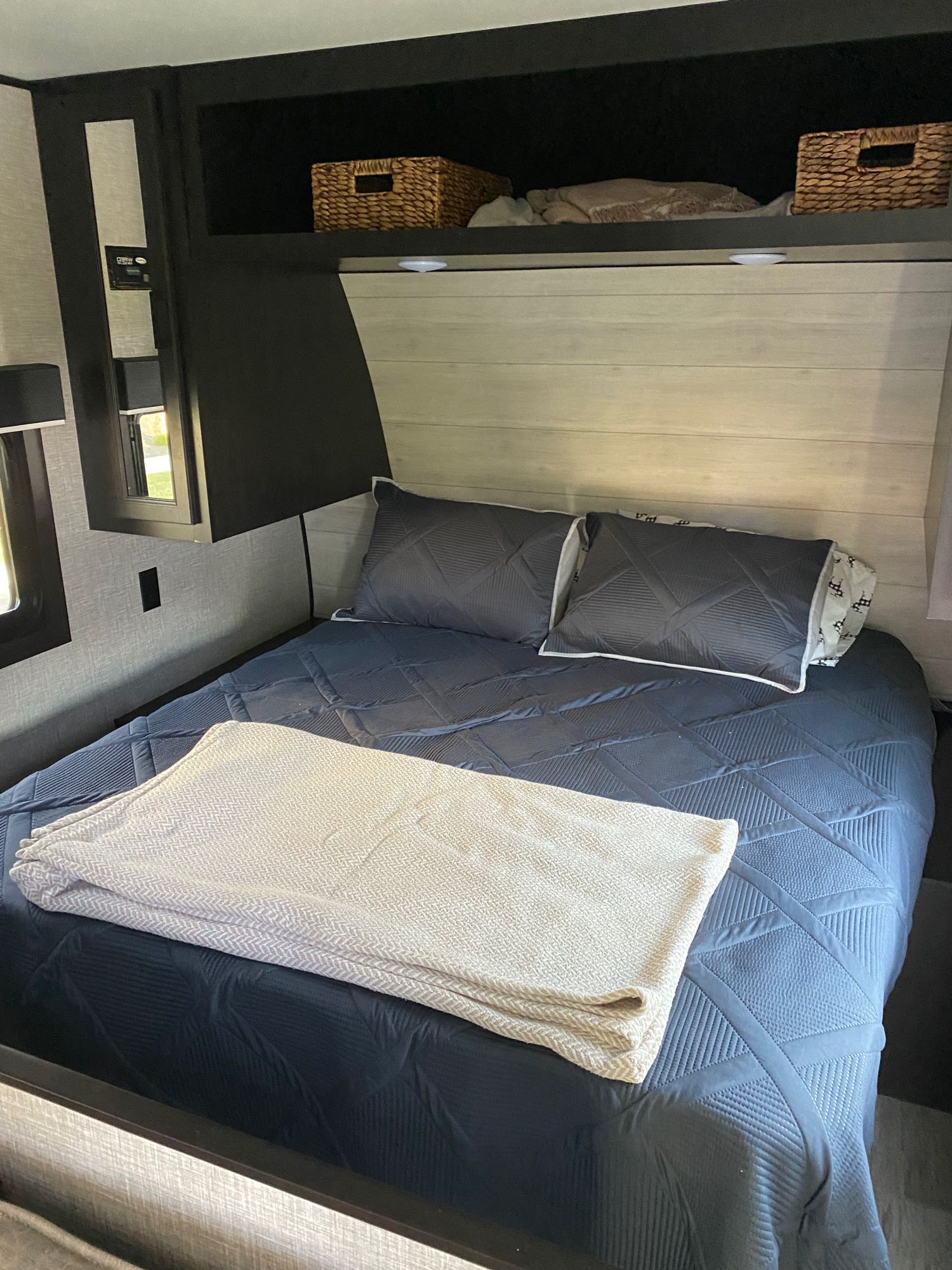 Inside a modern RV rental, a compact bedroom features a bed with blue bedding, pillows, and overhead storage.. Jayco Jay Flight 2023
