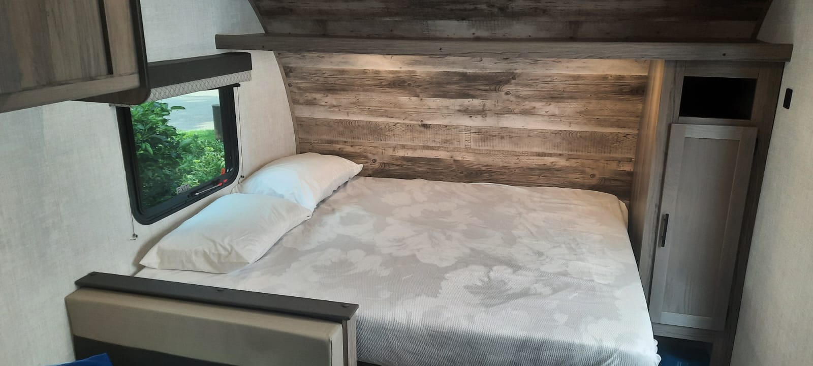 Cozy RV rental bedroom featuring a comfortable bed, rustic wood-look wall, and window. Perfect for your next adventure.. Grand River 19BH 2022