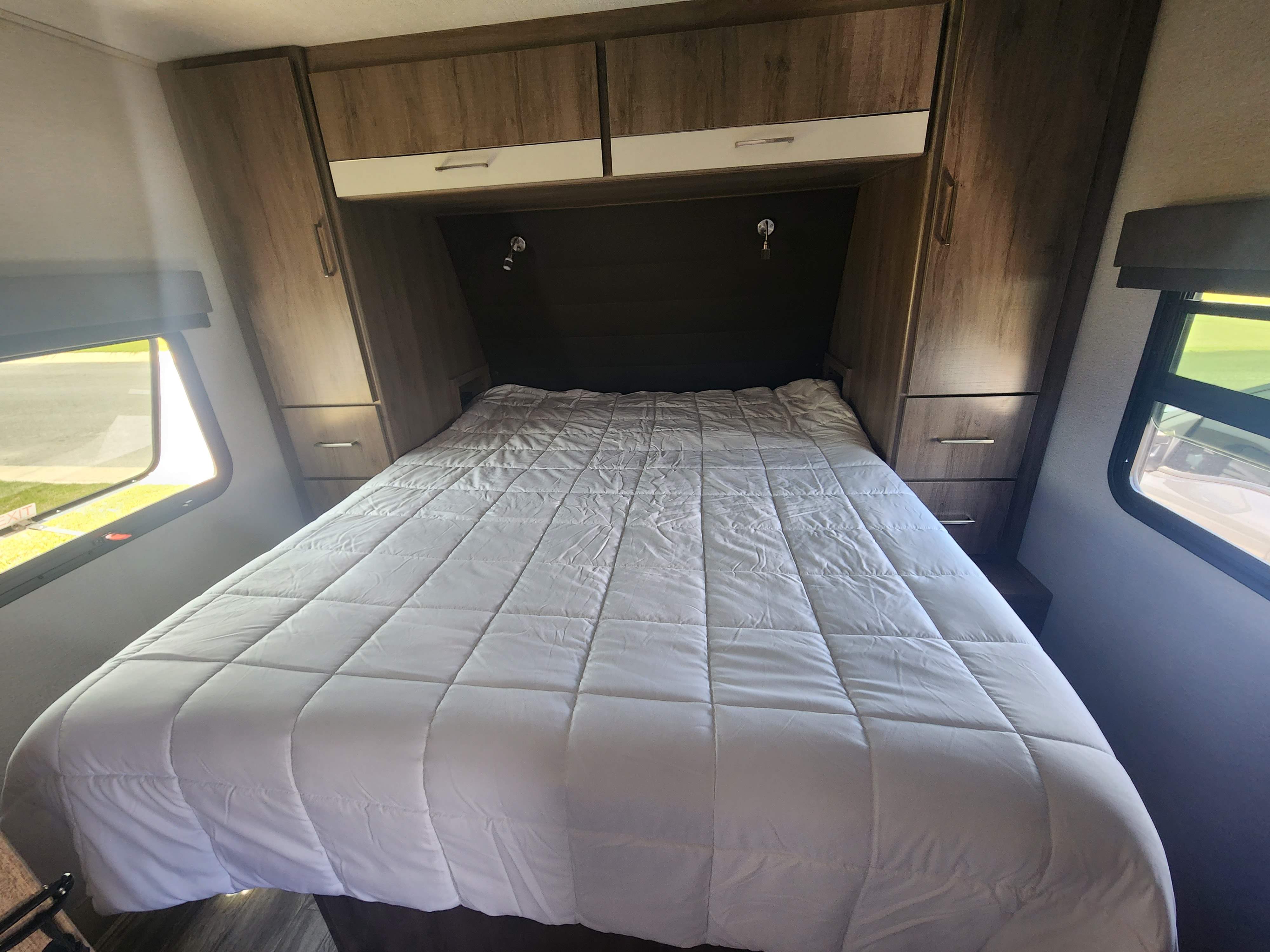 RV rental bedroom: spacious interior featuring a white bed, wood cabinets, and large windows with blinds.. Grand Design Imagine XLS 2022