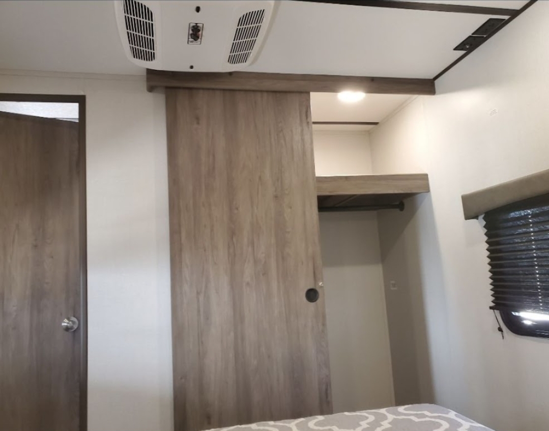 Explore this RV rental's bedroom, featuring a wood-grain sliding barn door, integrated closet, and overhead AC.. Crossroads RV Zinger 2020
