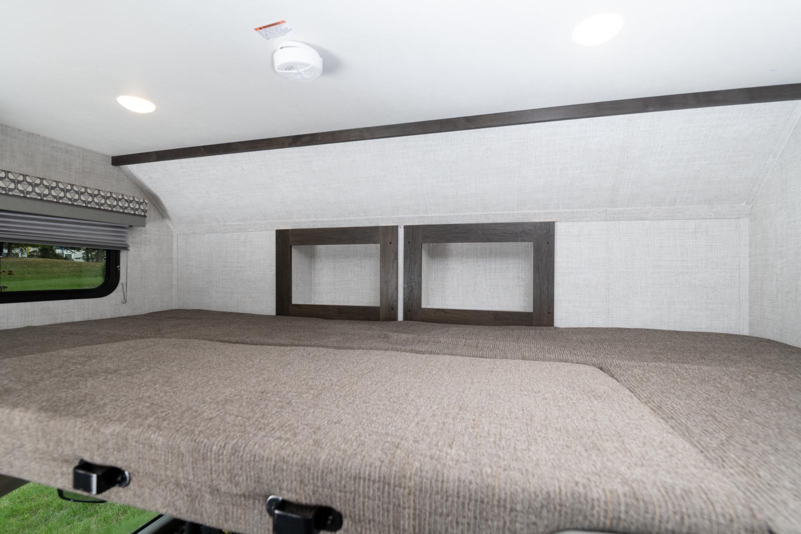 Spacious bed area in an RV rental, featuring overhead cubbies, a window, and neutral decor.. Gulf Stream Conquest 2024