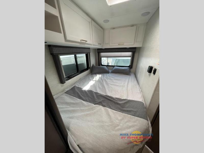 Experience comfort in this RV rental bedroom: a cozy bed with pillows, dual windows, and ample overhead storage.. Thor Chateau 2023