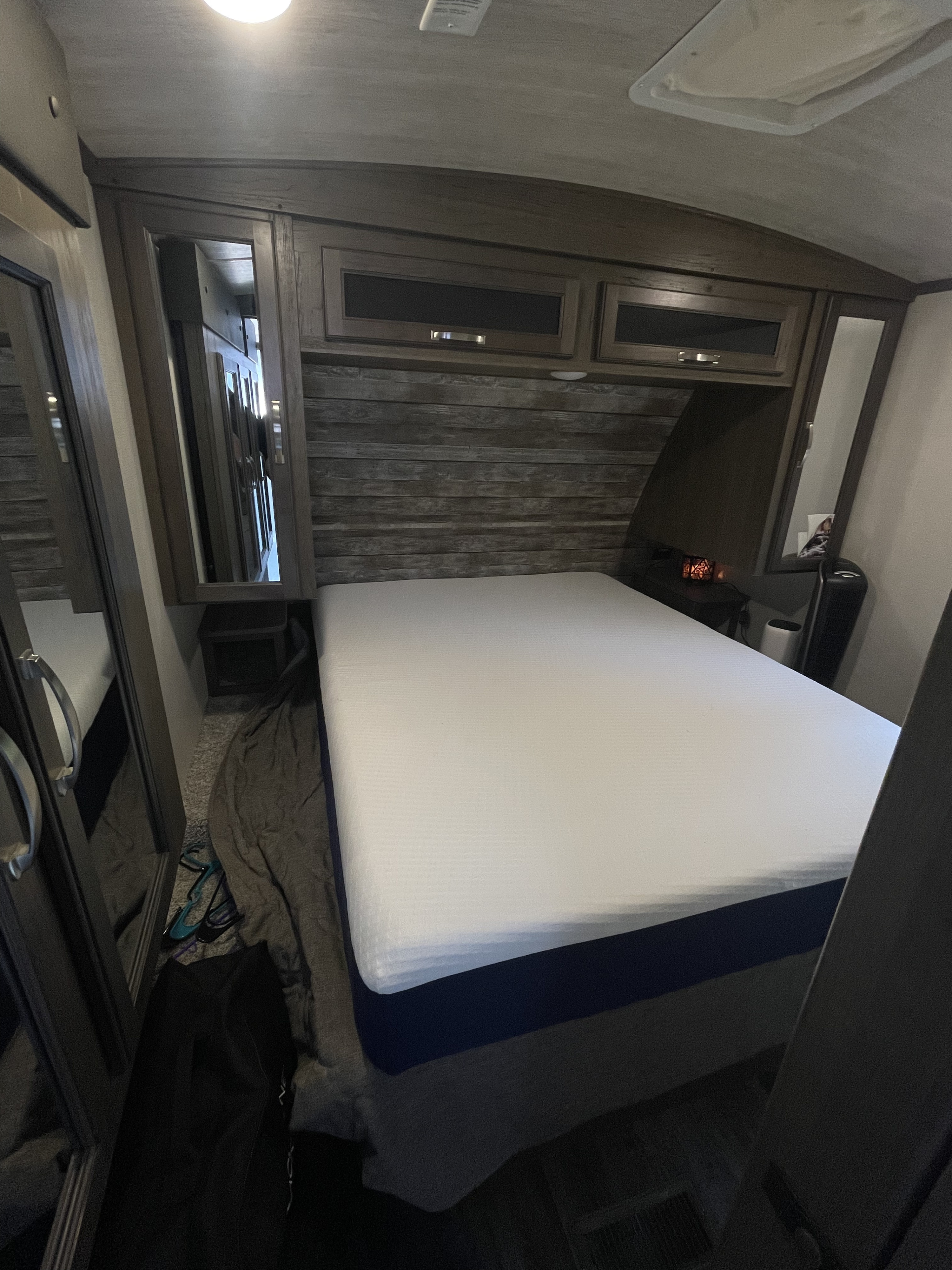 This inviting RV rental bedroom features a comfy bed, wood-paneled headboard, overhead cabinets, and mirrored storage.. Keystone RV Cougar 2022