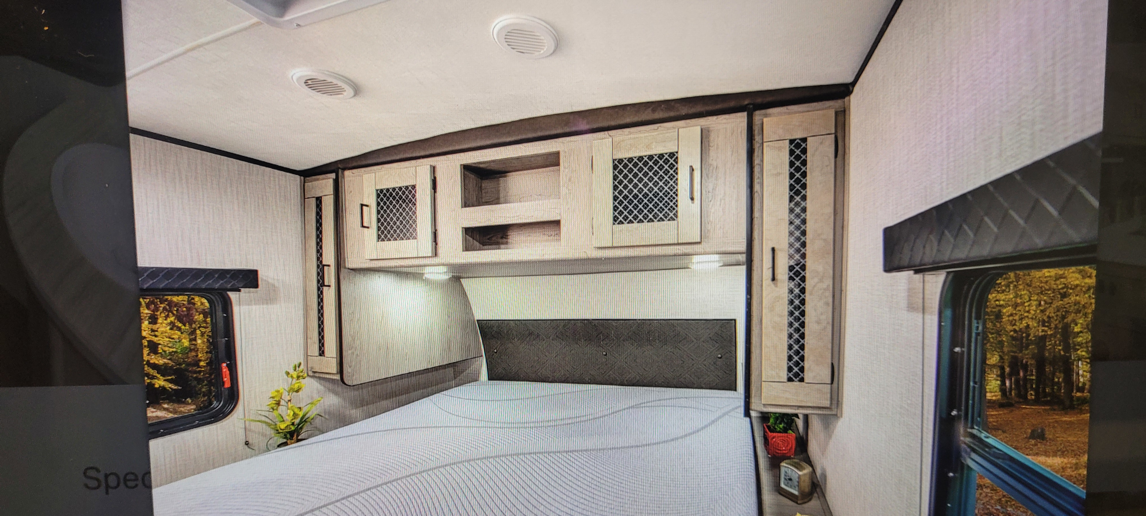 RV rental bedroom with overhead cabinets, a comfortable bed, and windows offering a scenic view of autumn trees.. Heartland RVs Mallard 2022