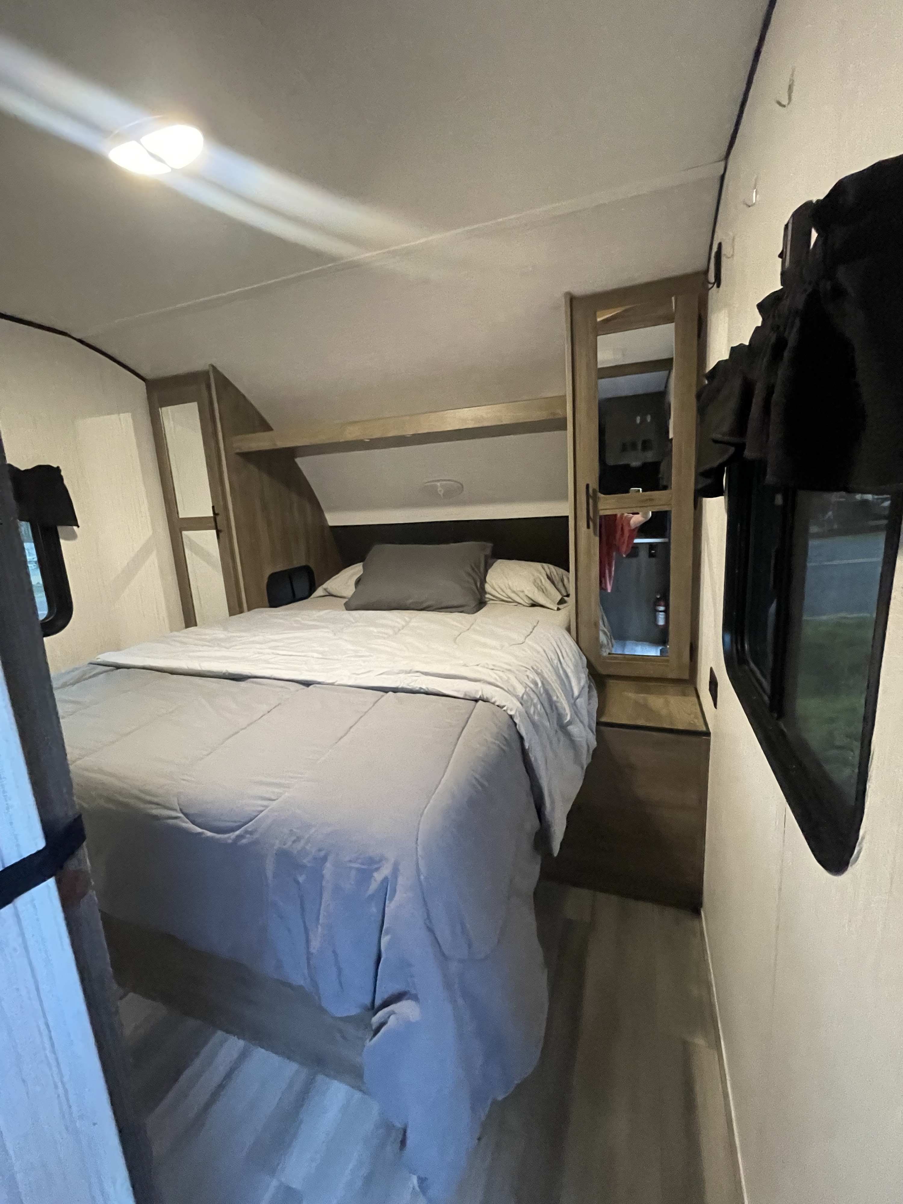 Cozy RV rental bedroom featuring a queen bed with light bedding, ample overhead storage, mirrored closet, and window blinds.. Heartland RVs Pioneer 2021