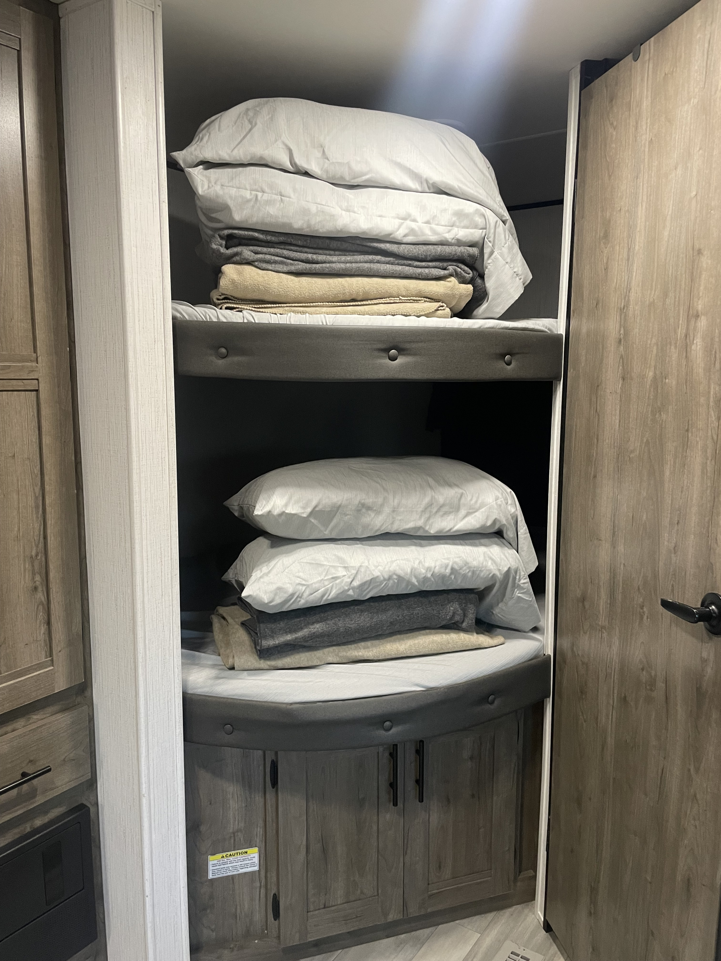 Cozy RV rental bunk beds with pillows and blankets stacked on top, nestled within wooden cabinetry.. Heartland RVs Pioneer 2021