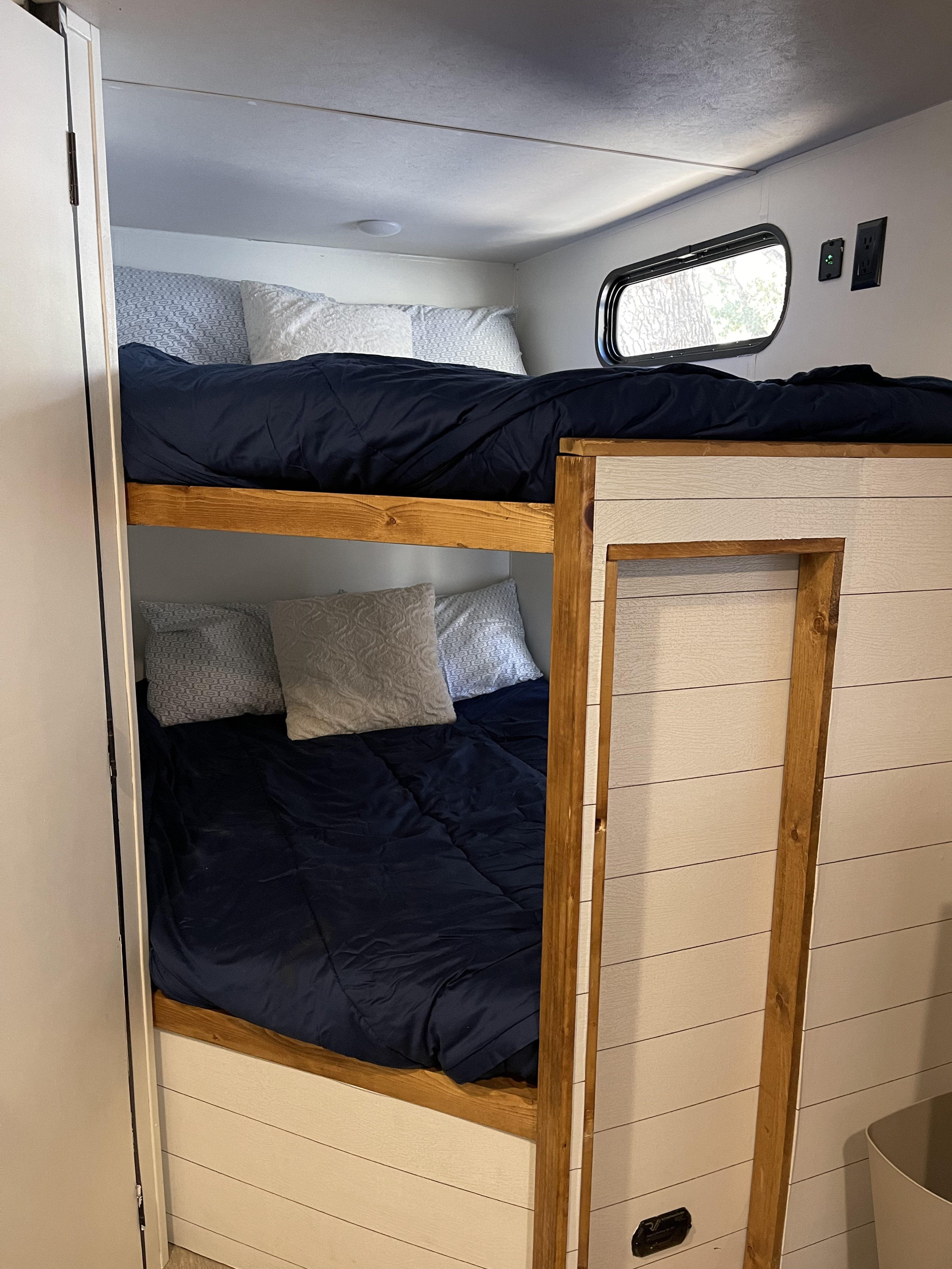 RV rental's cozy bunk beds featuring dark blue bedding, wooden frames, and white shiplap walls.. Forest River Cherokee Grey Wolf 2021