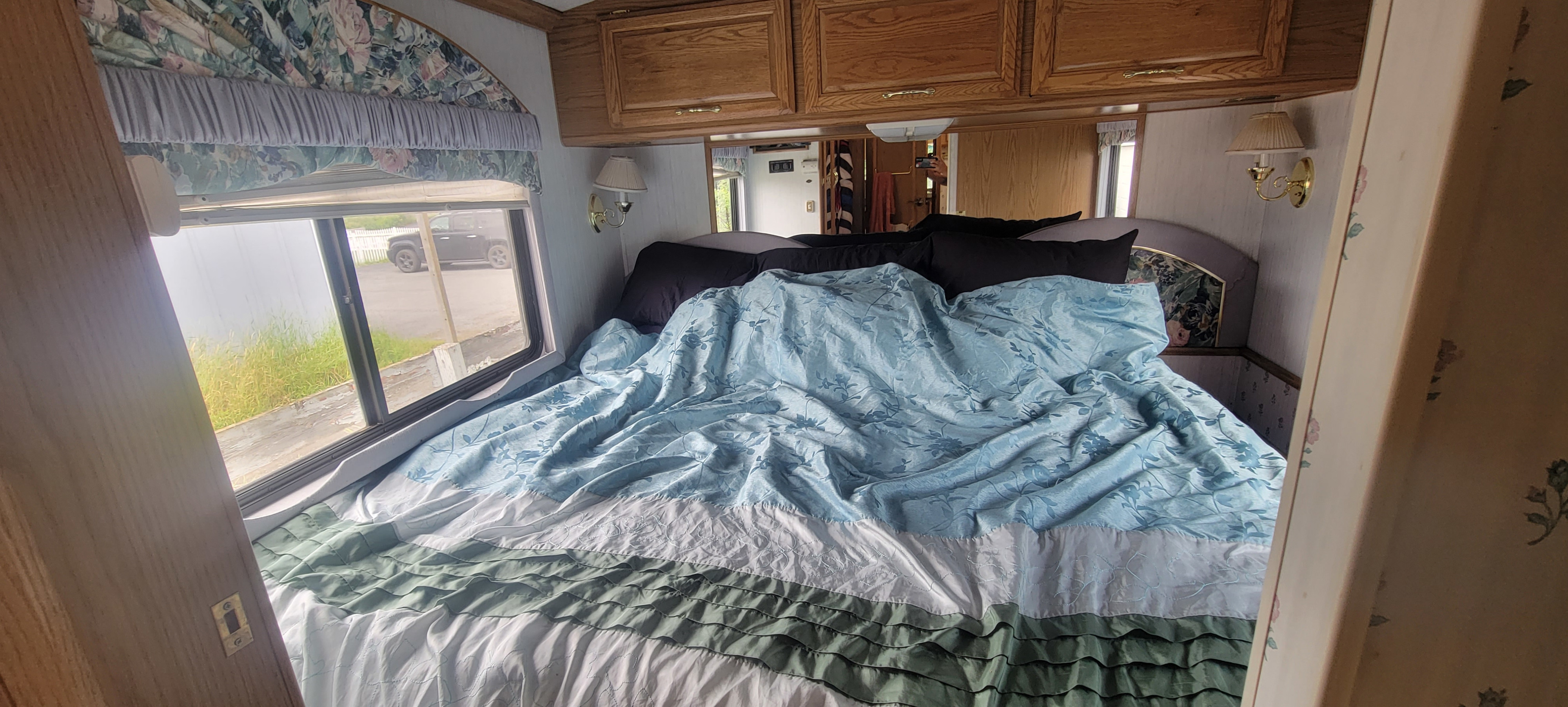 Comfortable rv rental bedroom showcasing a bed with blue floral comforter, ruffled skirt, and exterior window view.. Pace-Arrow 35' 1996
