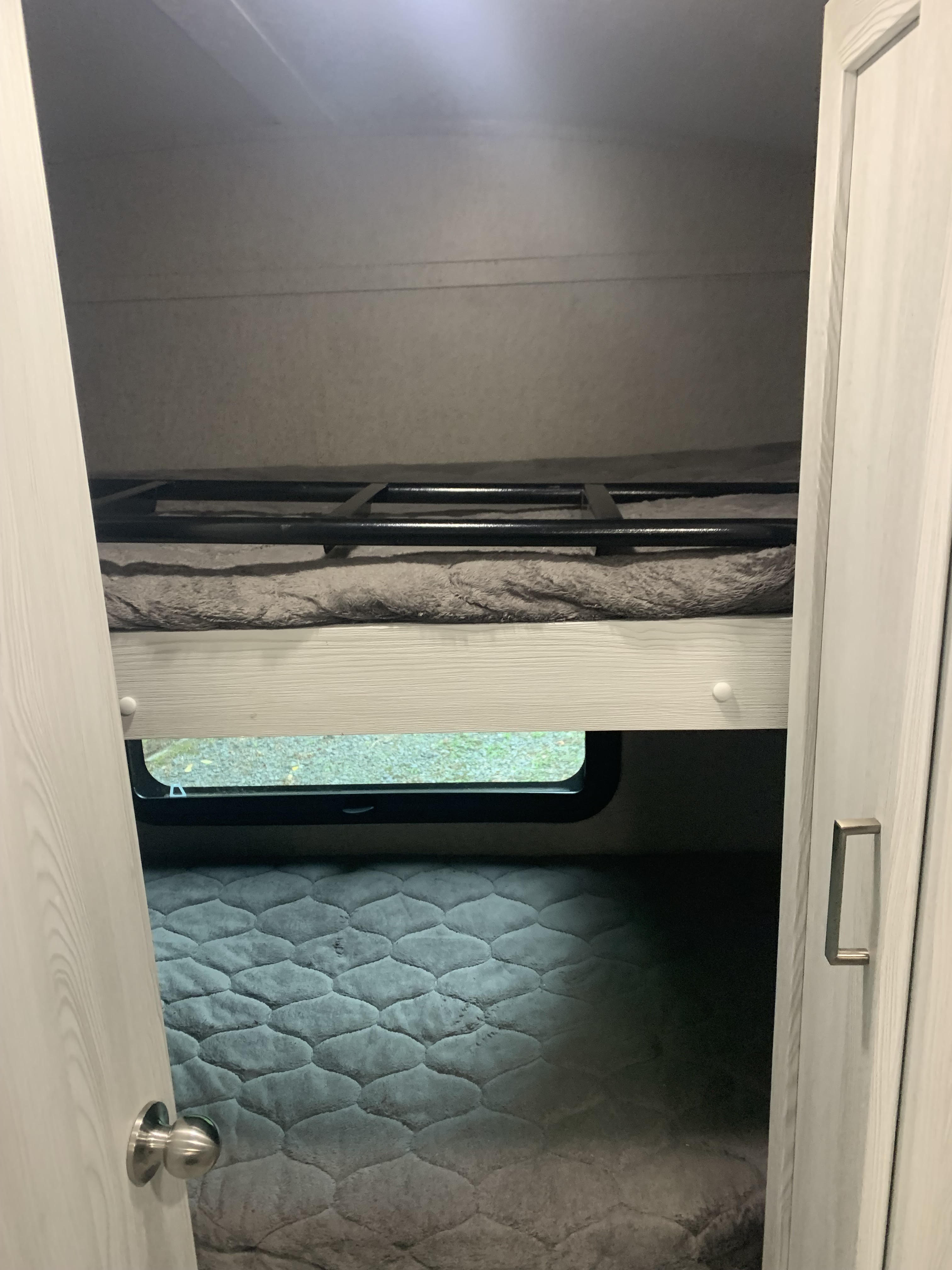 Cozy bunk beds inside an RV rental, featuring an upper bunk with a safety rail and a lower bunk beside a small window.. Forest River Rockwood Geo Pro 2020