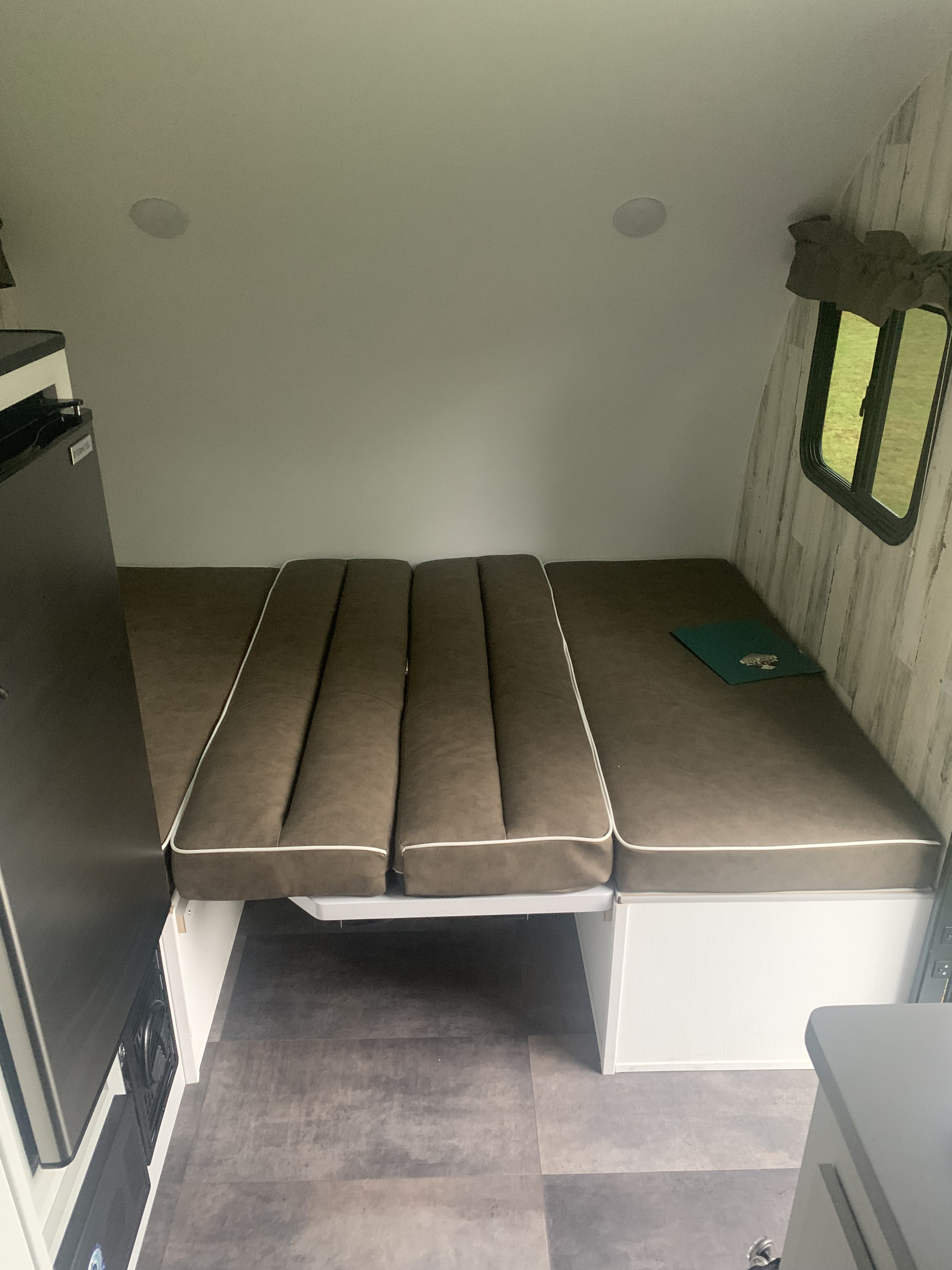 RV rental: Compact camper interior with brown upholstered bed/seating, compact refrigerator, and window view.. Travel Lite Rove 14BH 2024