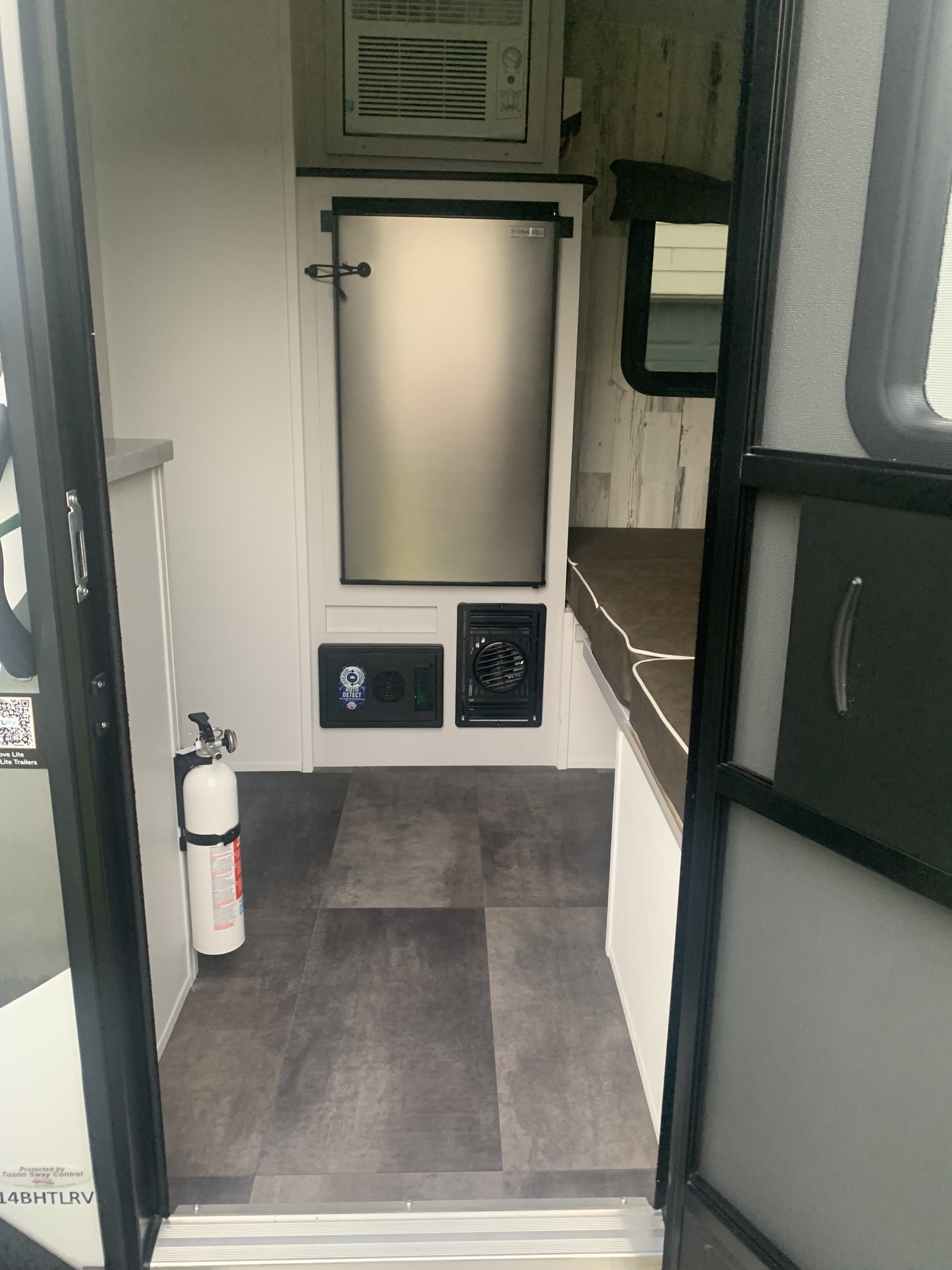 Compact RV rental interior with refrigerator, AC, and a fire extinguisher. Ideal for comfortable travel.. Travel Lite Rove 14BH 2024