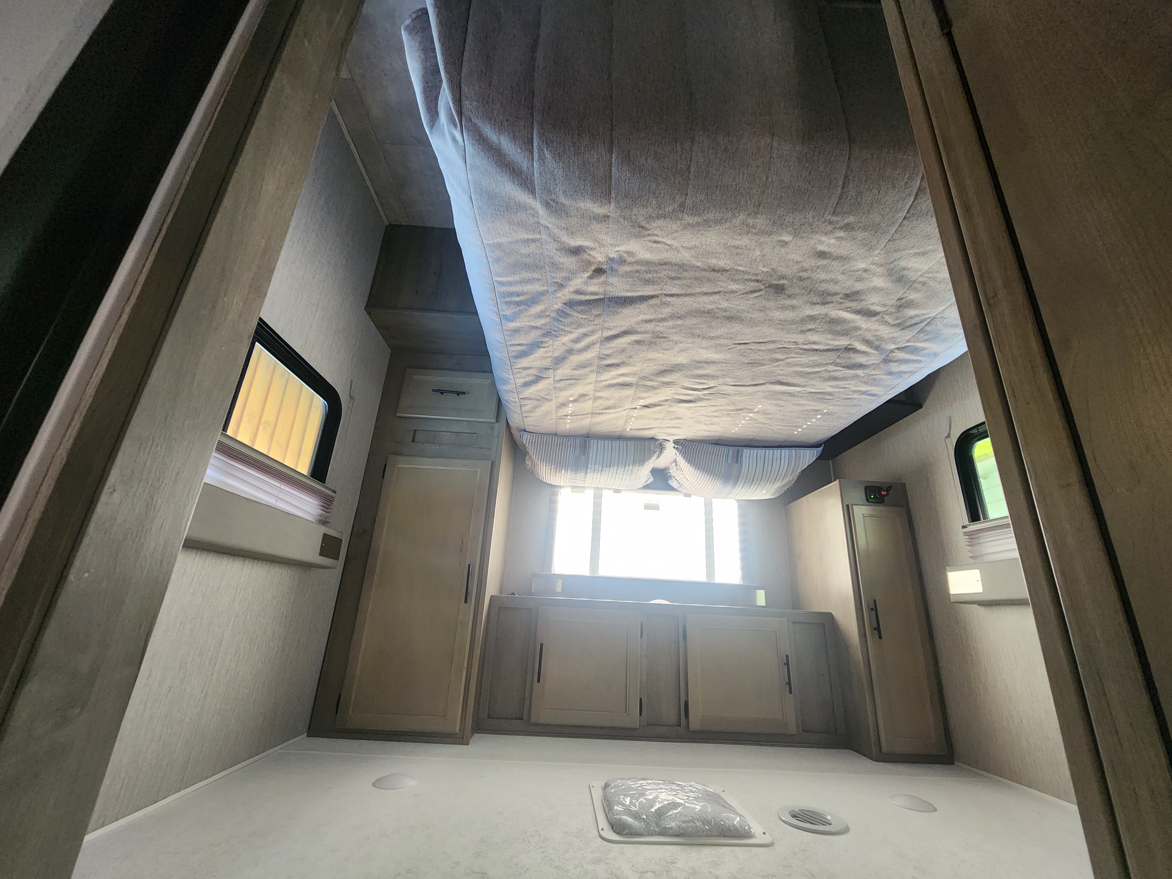 Interior of an RV rental: a bright, modern bedroom area with a raised bed, cabinets, and windows, viewed from the floor.. Coachmen Freelander 2023