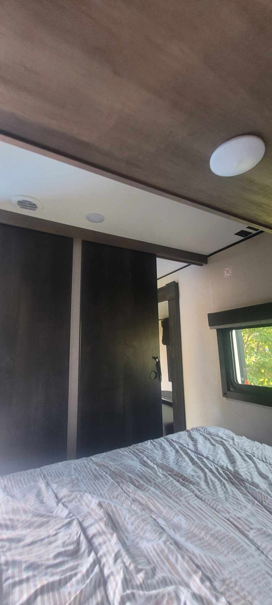 Cozy RV rental bedroom interior with patterned bedding, dark sliding doors, and a window showing greenery.. Starcraft Autumn Ridge 2022