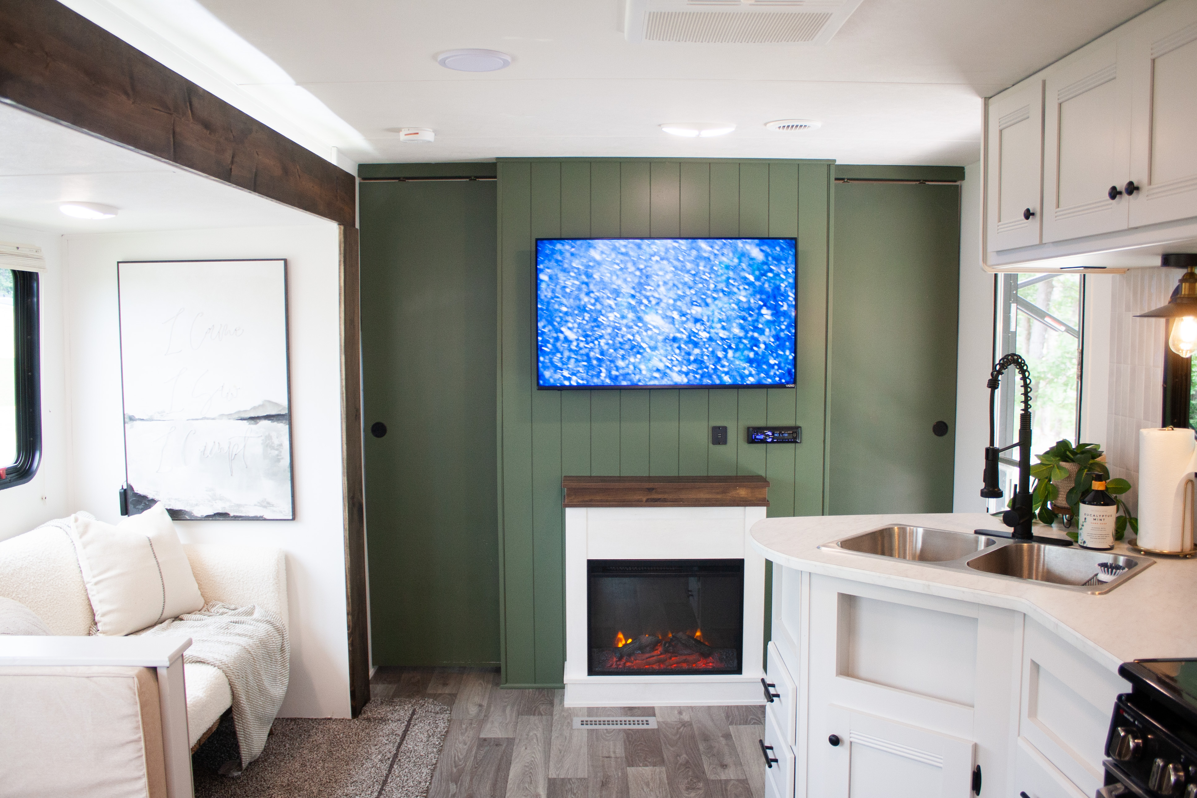 Stylish RV rental interior: green feature wall with TV & fireplace, white kitchen, cozy living space.. Heartland RVs Pioneer 2020