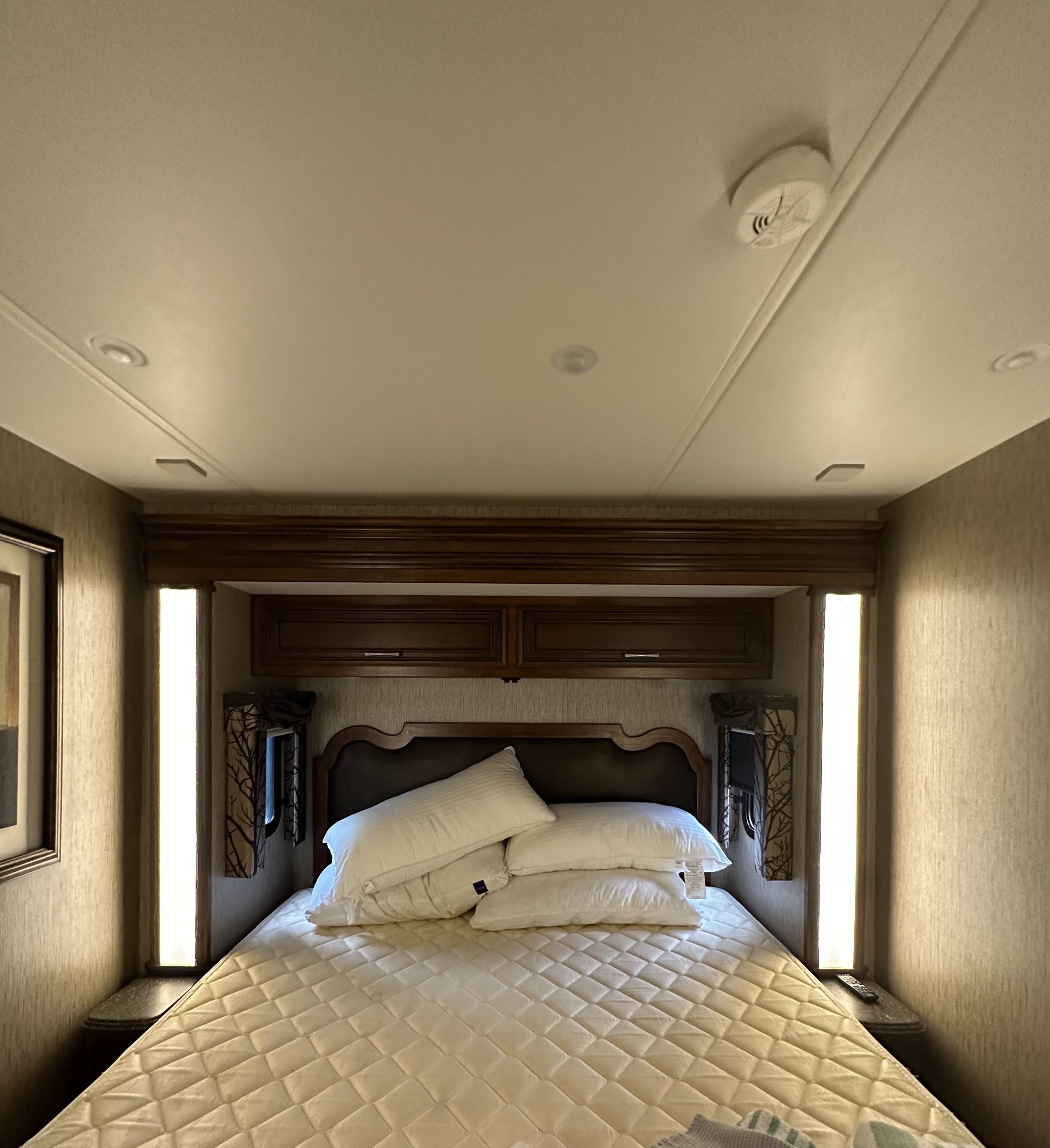 Cozy RV rental bedroom featuring a comfy bed with quilted cover, dark wood headboard, and bright side lighting.. Newmar Canyon Star 2016