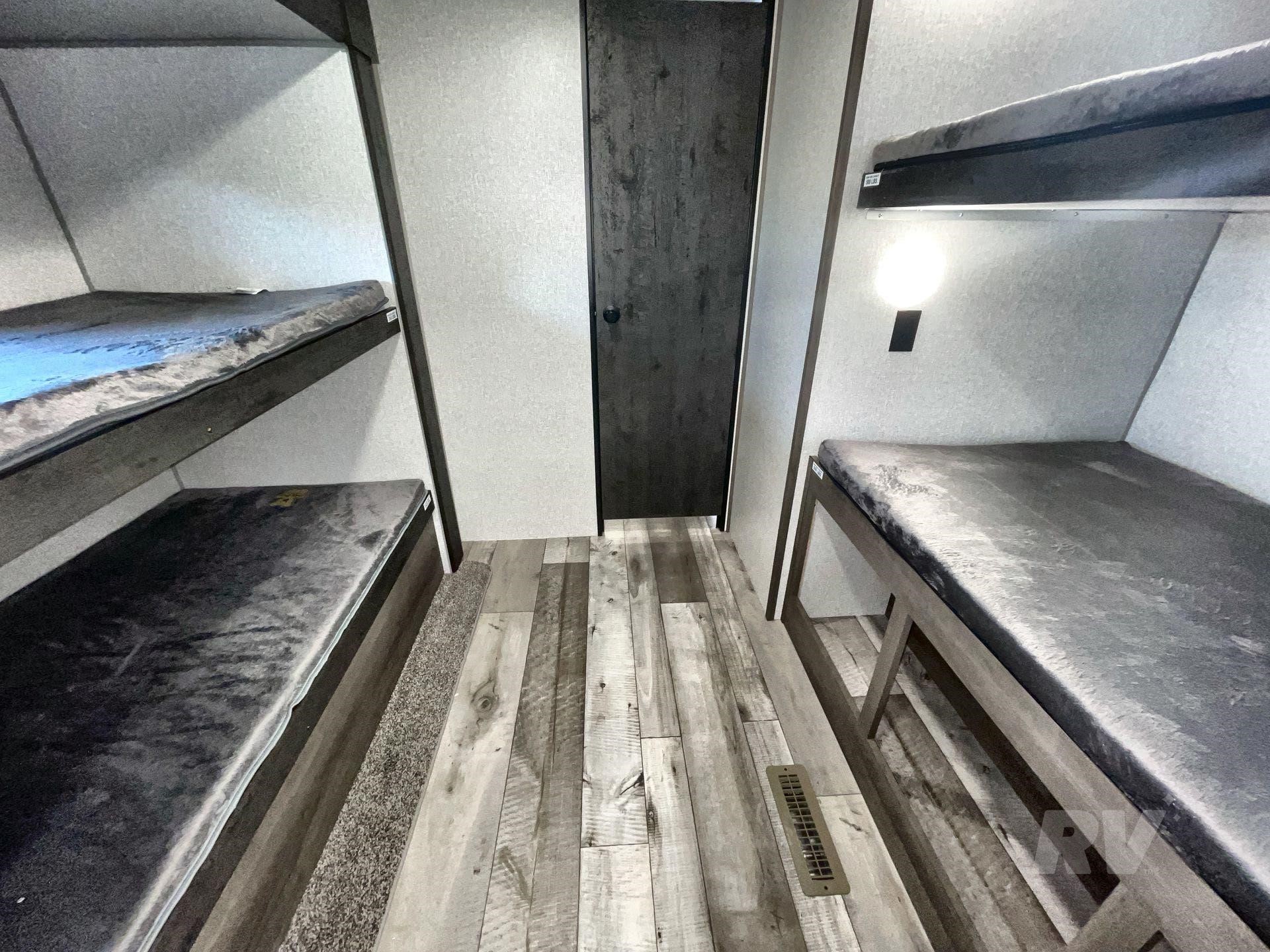 RV rental bunkhouse: Interior of an RV with two sets of grey bunk beds, a central aisle, and a dark door at the end.. KZ Sportsmen SE 2021