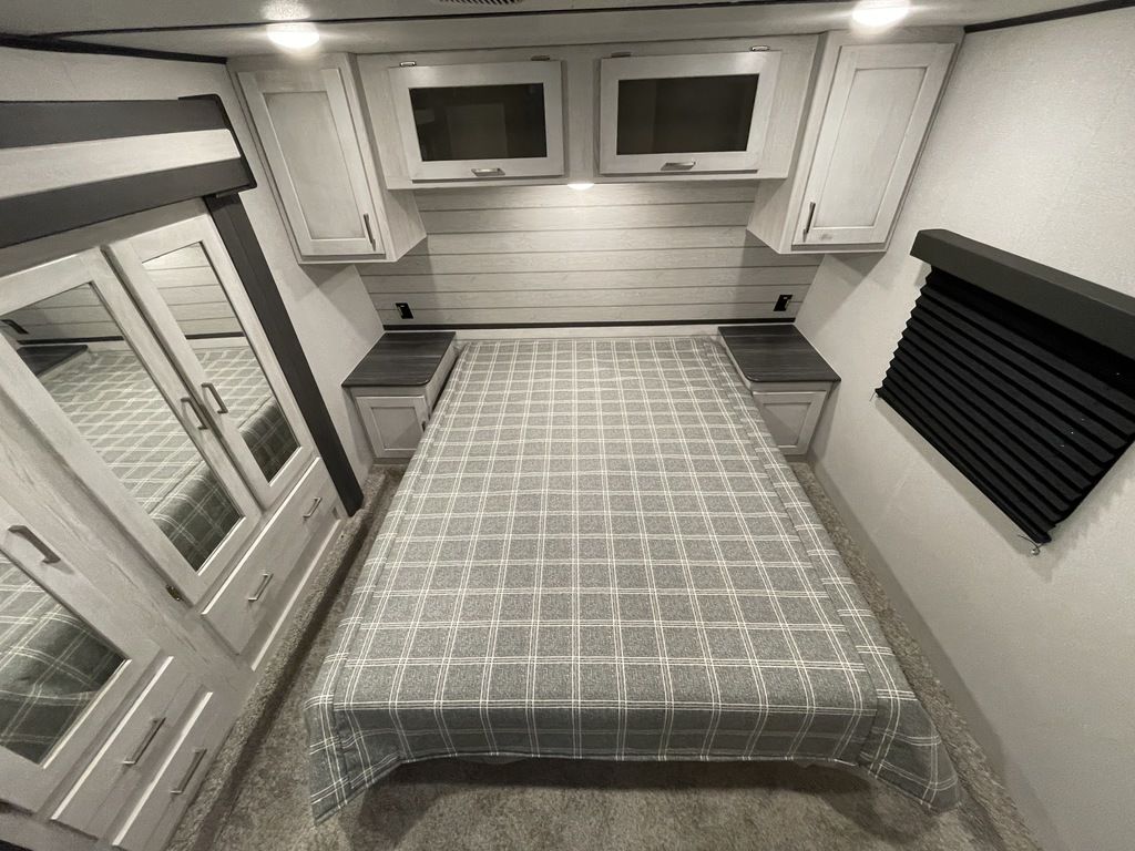 Inside an RV rental, a cozy bedroom with a plaid bed, mirrored closet, overhead storage, and side nightstands.. Keystone Sprinter 2022