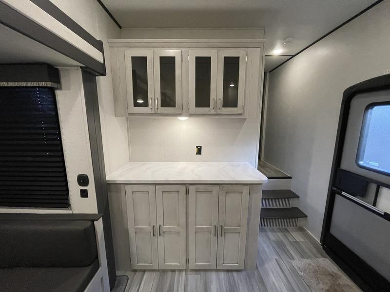 Modern RV rental interior: light wood cabinets, versatile counter, bunk, and steps leading to another section.. Keystone Sprinter 2022