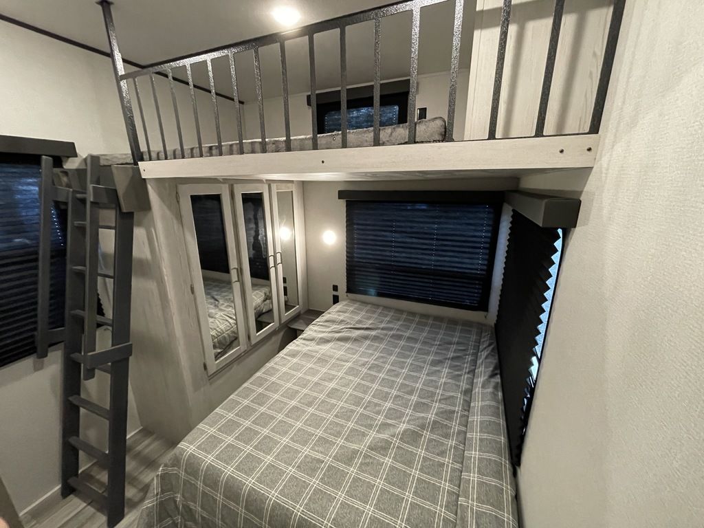 Spacious RV rental interior showcasing a lower bed, bunk bed ladder, and an upper sleeping loft with railing.. Keystone Sprinter 2022
