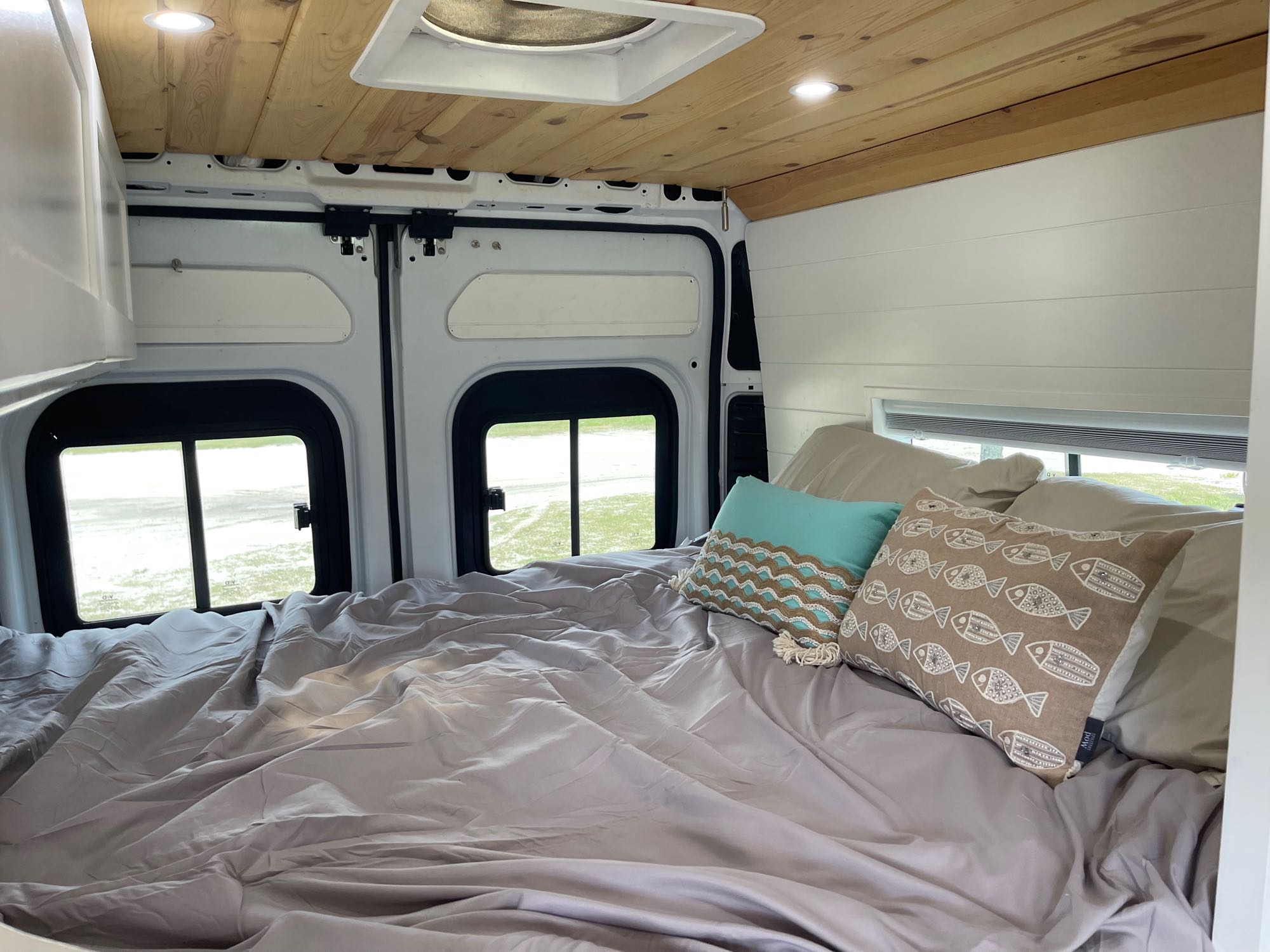 Cozy RV rental camper van bed setup with wood ceiling, white walls, and comfy pillows, perfect for adventures.. Dodge Pro Master 2021