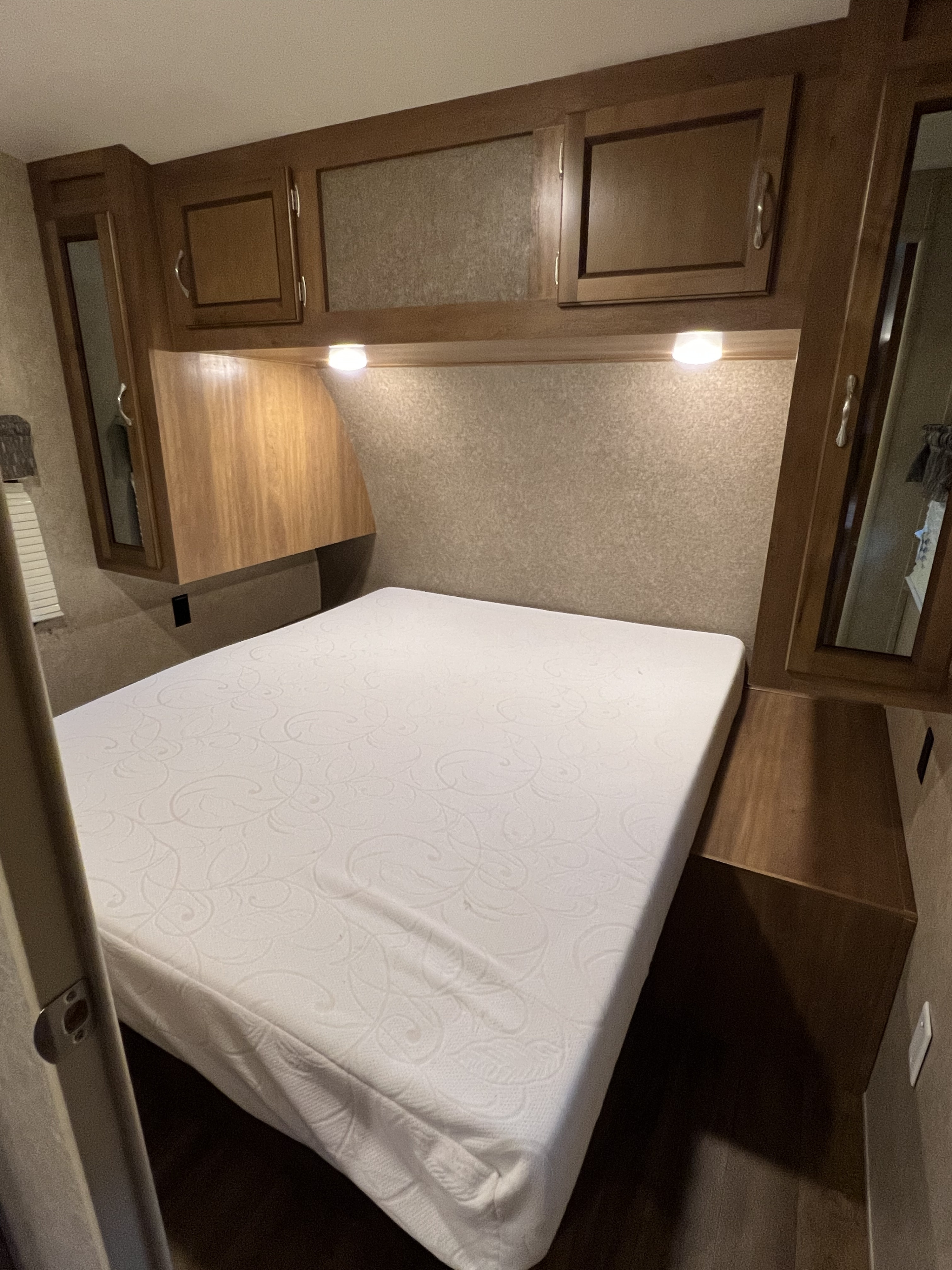 Compact RV rental bedroom featuring a clean white mattress, overhead storage cabinets, and functional lighting.. Coachmen Catalina 2017