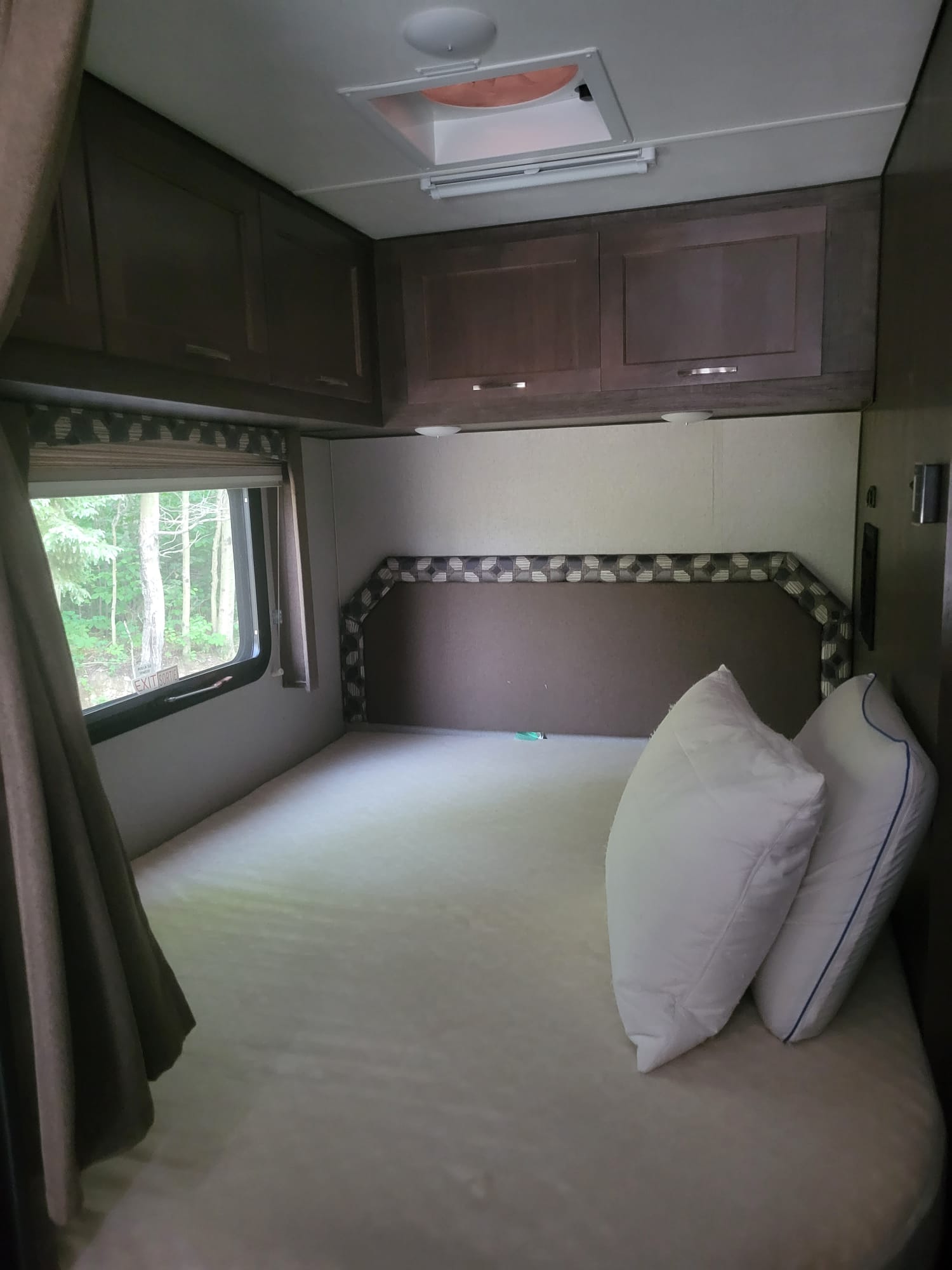 Experience comfort in this **rv rental** bedroom: bed with pillows, overhead cabinets, and a window with a natural view.. Adventurer Adventurer Motorhome 2019