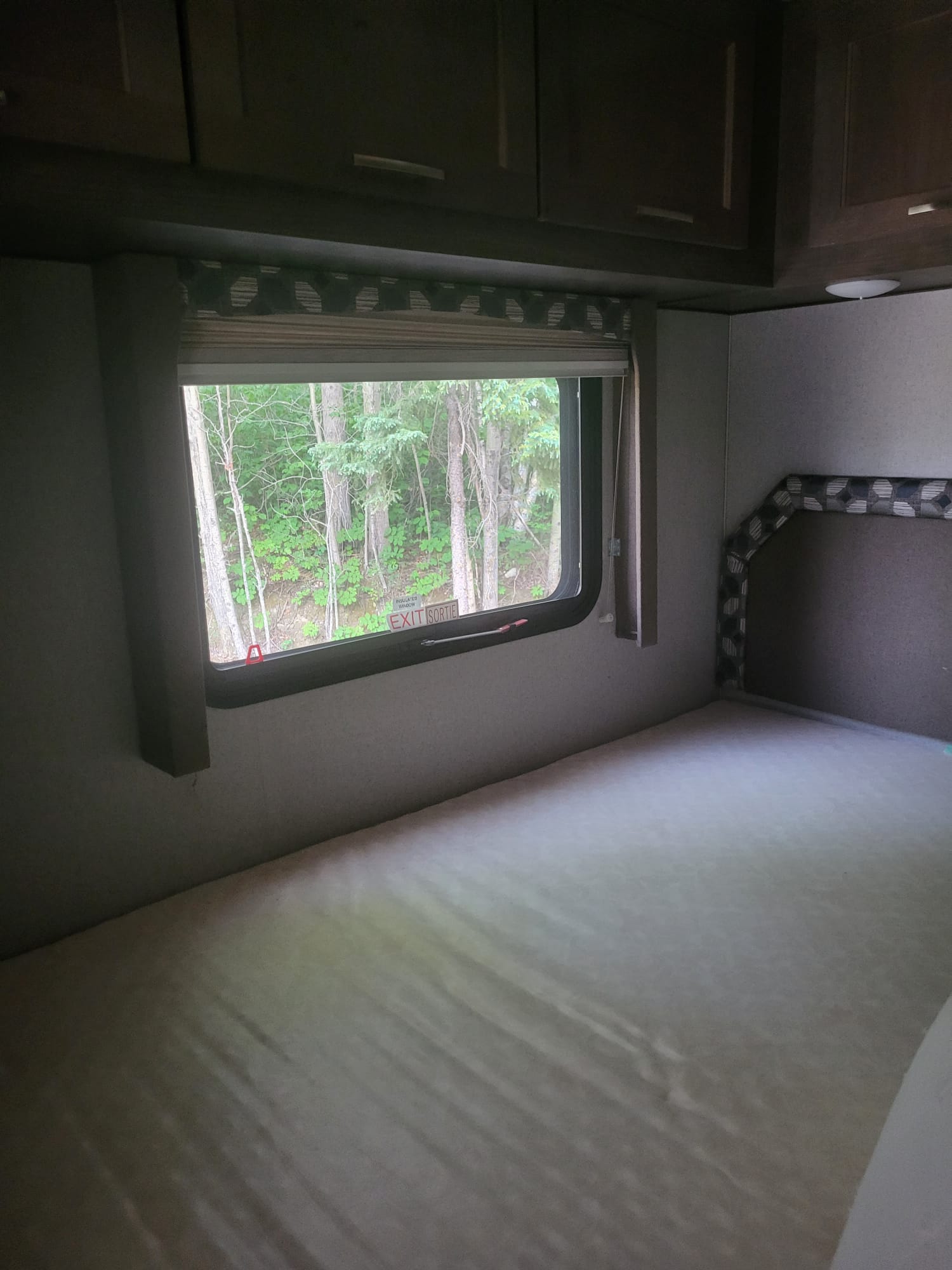 RV rental interior: A bedroom with a bed, window looking out to a forest, and overhead cabinets.. Adventurer Adventurer Motorhome 2019
